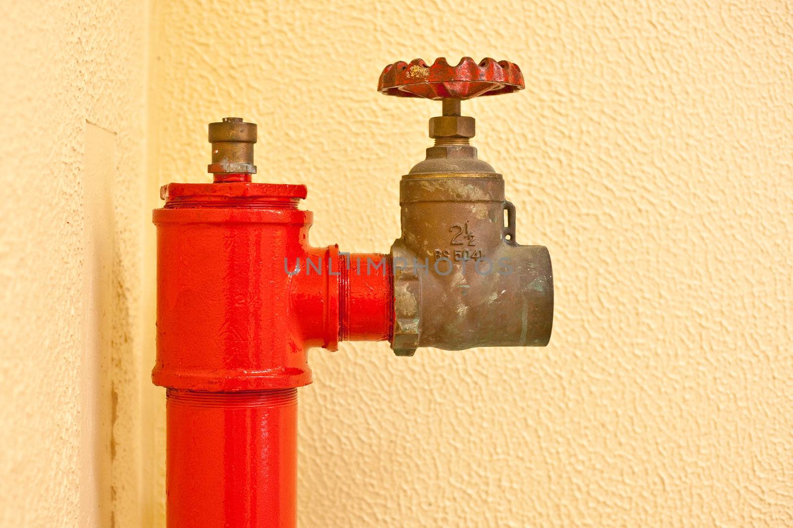 Red fire hydrant against a yellow wall