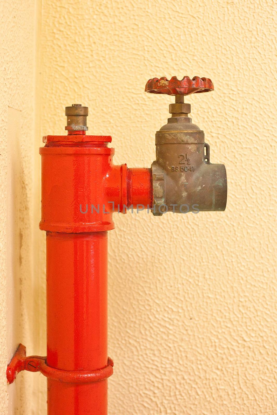 A vibrant red fire hydrant against a yellow wall