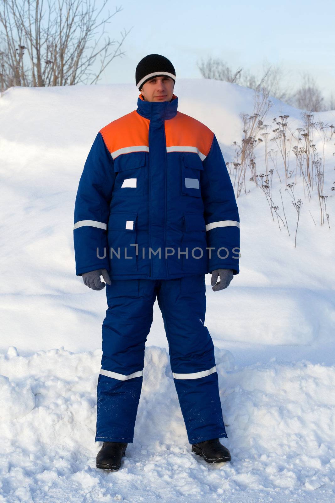 Worker in the winter suit consisting of a jacket and trousers against the backdrop of the snow