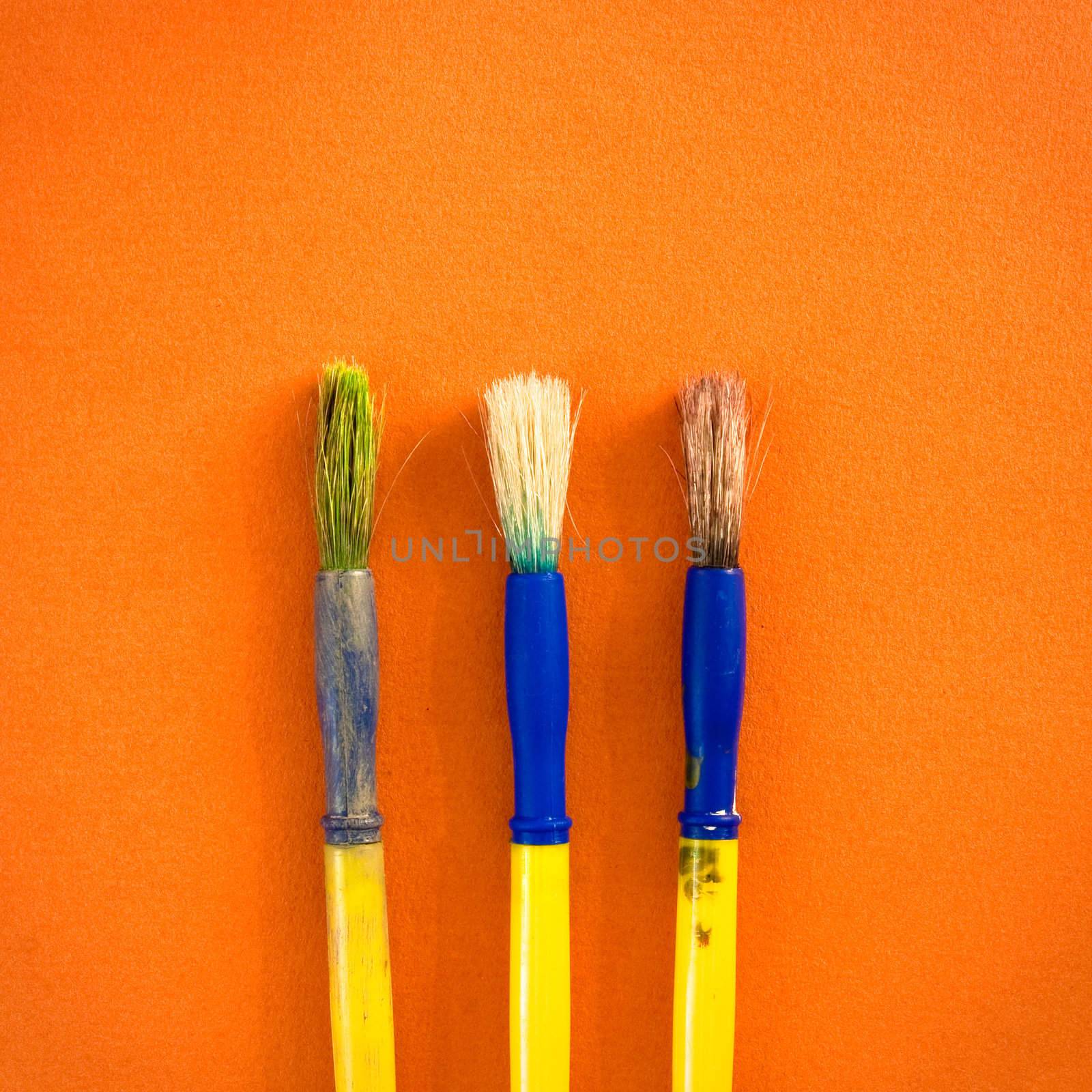 Three used paint brushes on an orange background