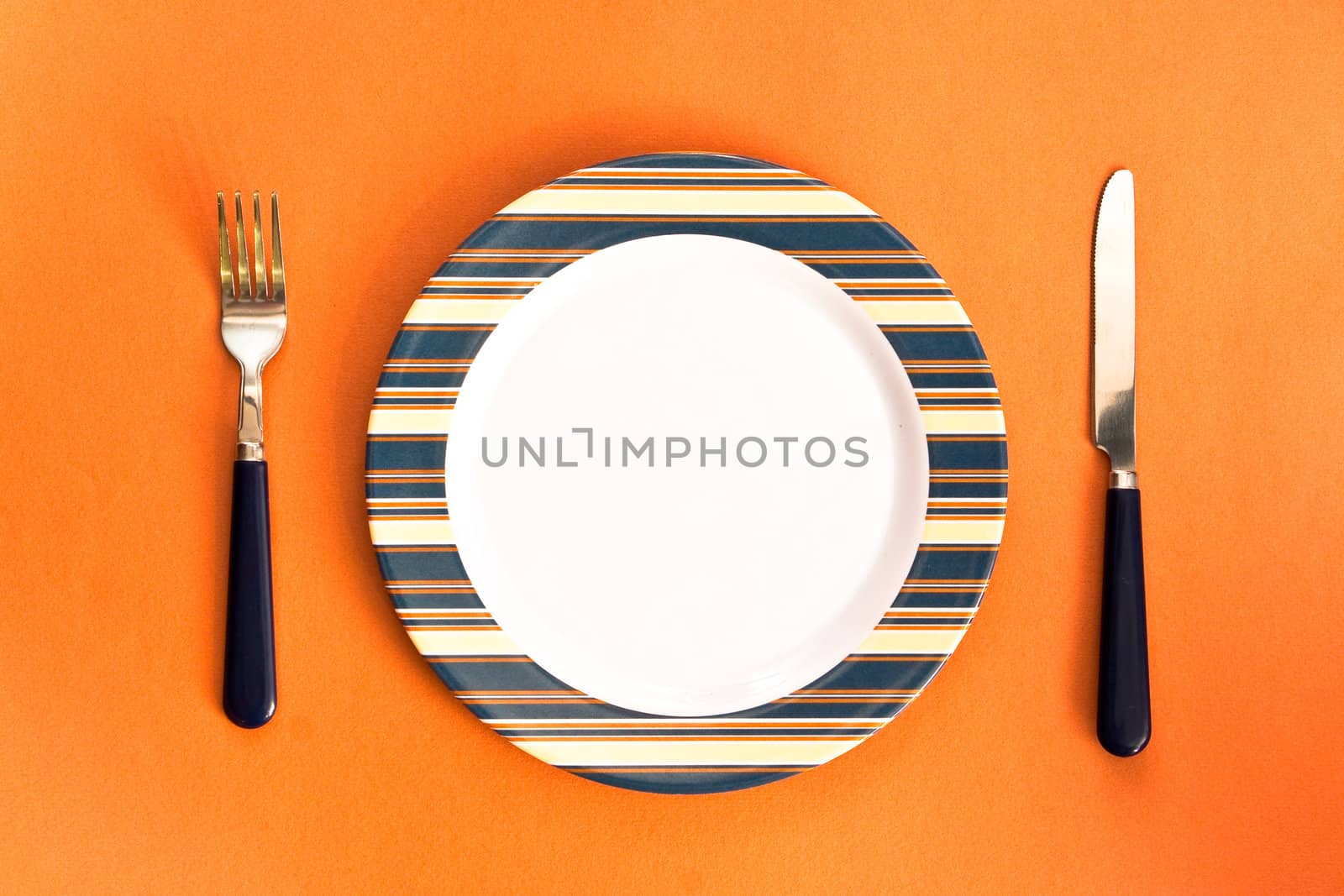 Nice image of a plate with a knife and fork on orange surface