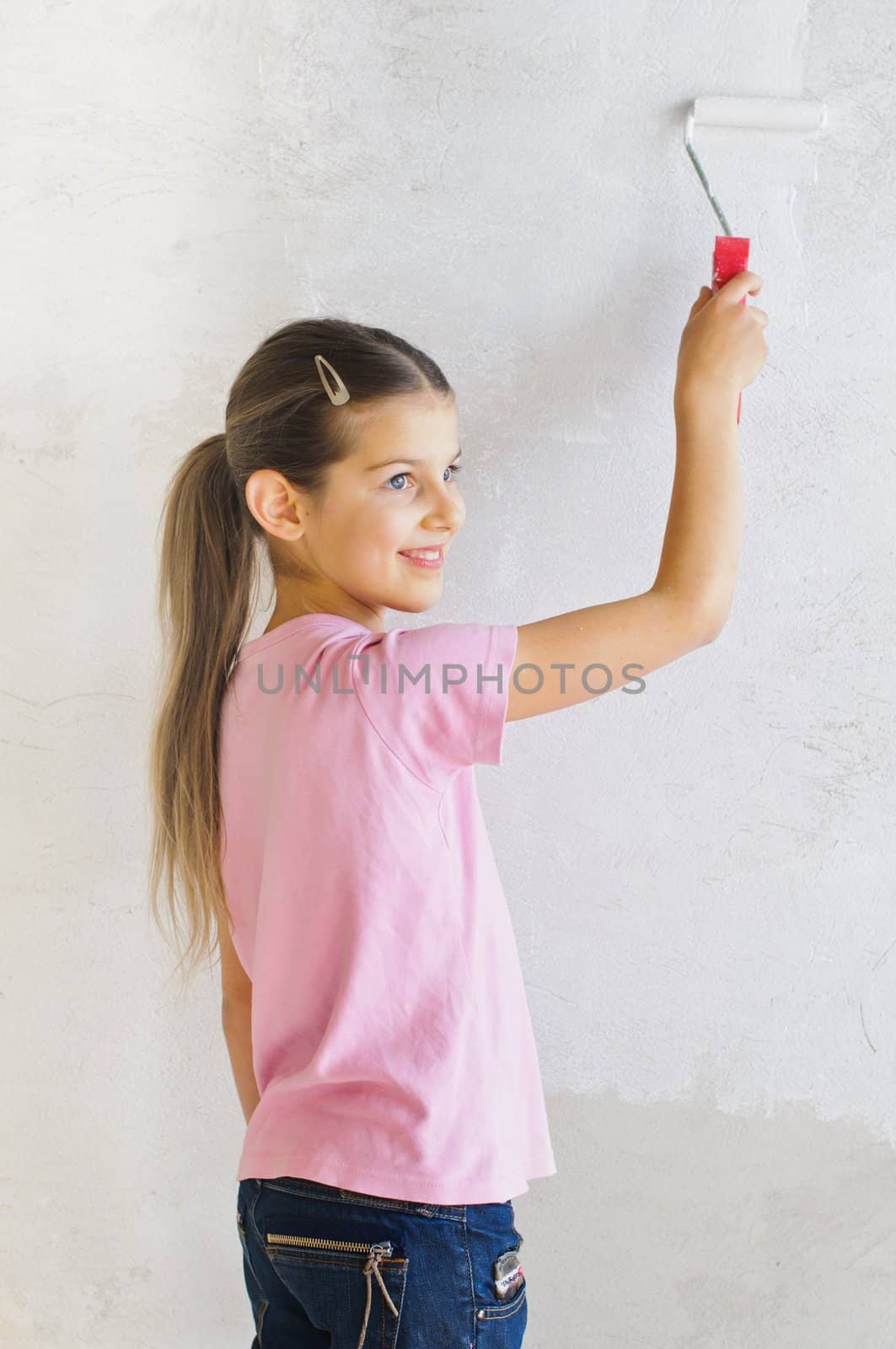 Happy beautiful girl painting a wall with roller