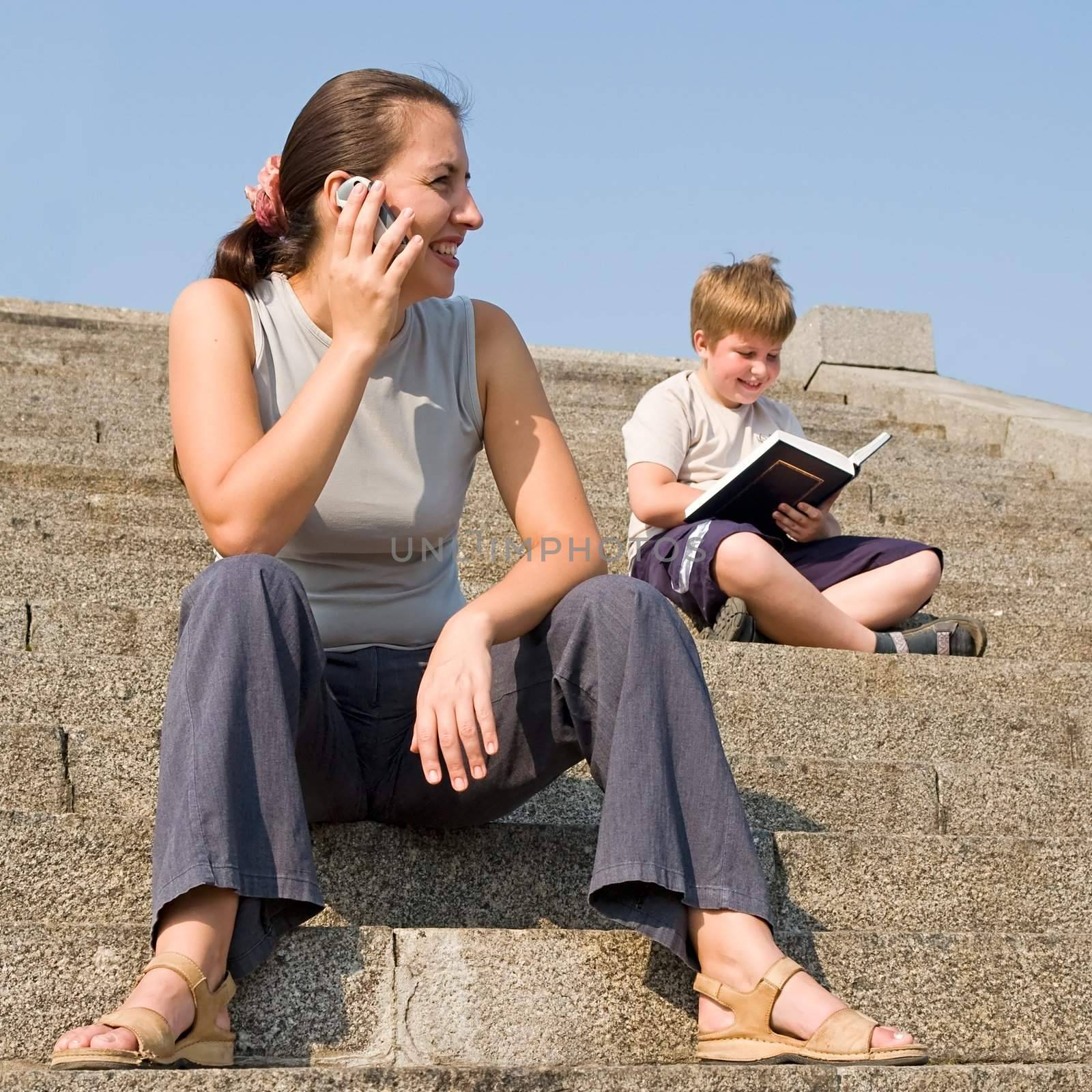 girl with mobile phone on a stone staircase. boy reads book