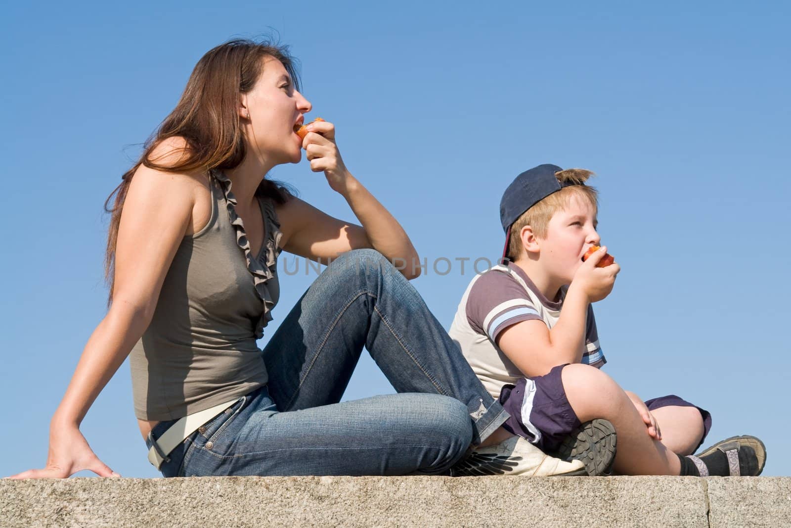 Mum and the son eat peaches with sky at background