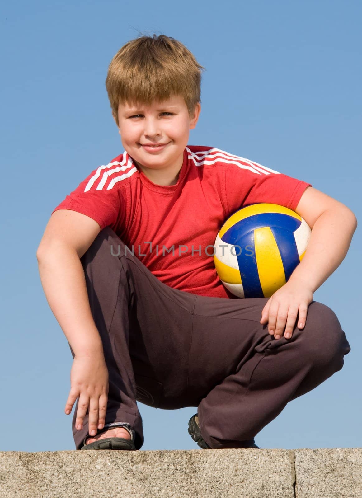 sitting boy with volleyball ball on a blue sky