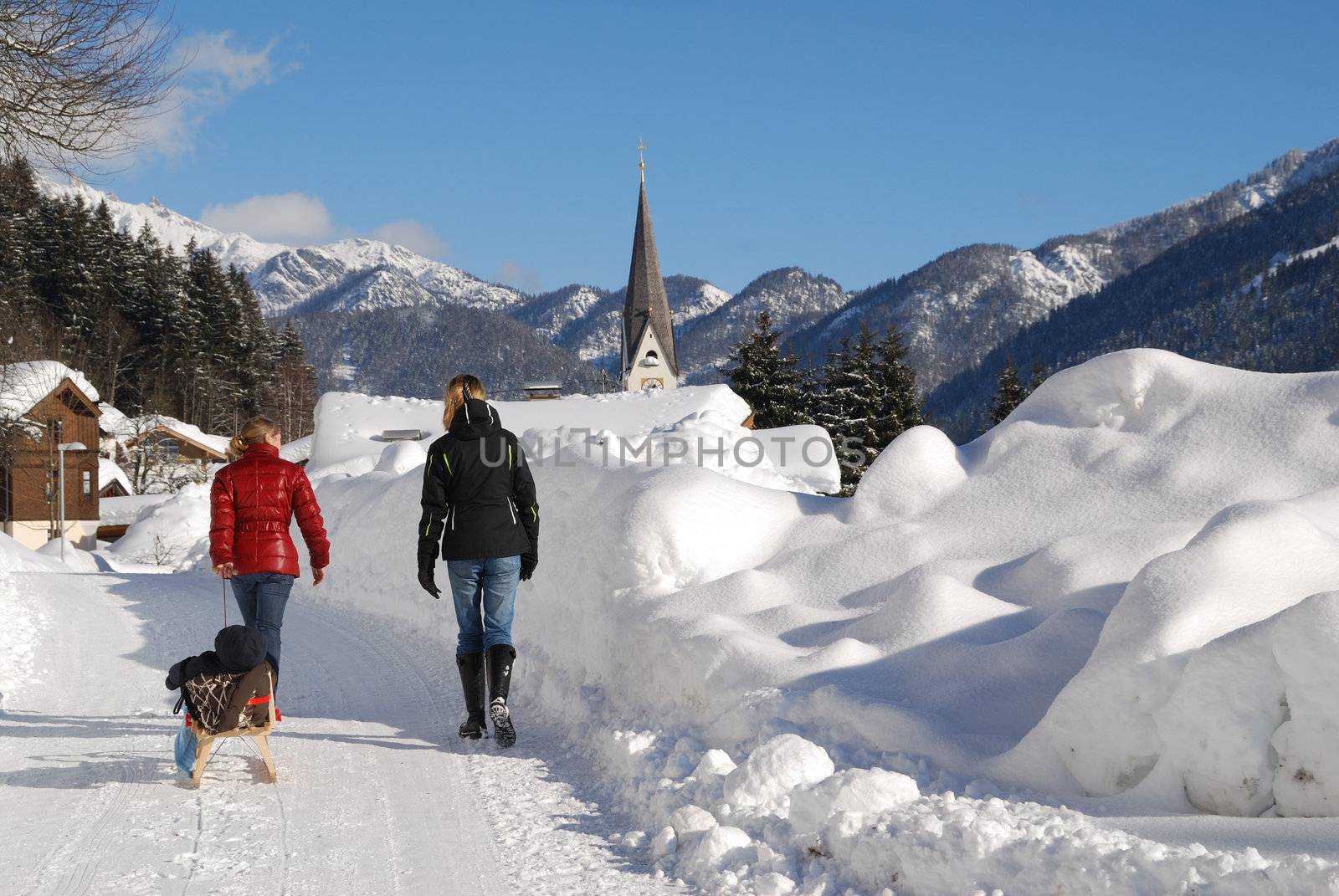 Young women with baby in sleigh walking in snow covered landscape in austria.