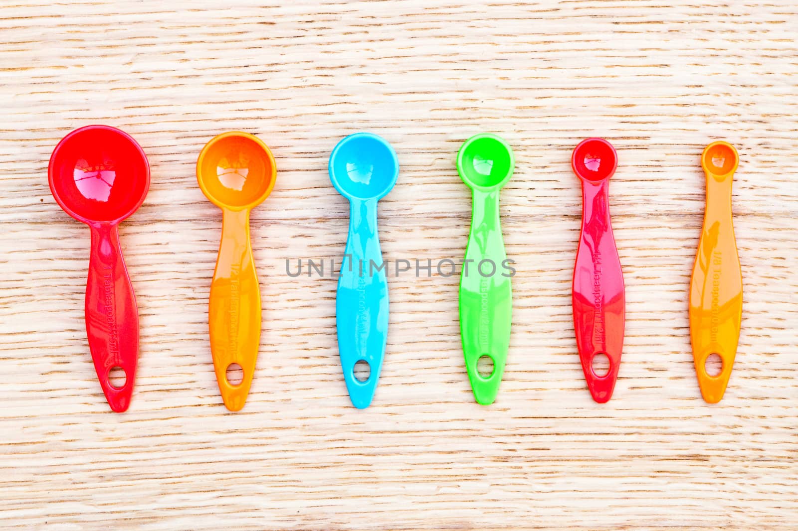 Group of six colorful measuring spoons on a wooden surface