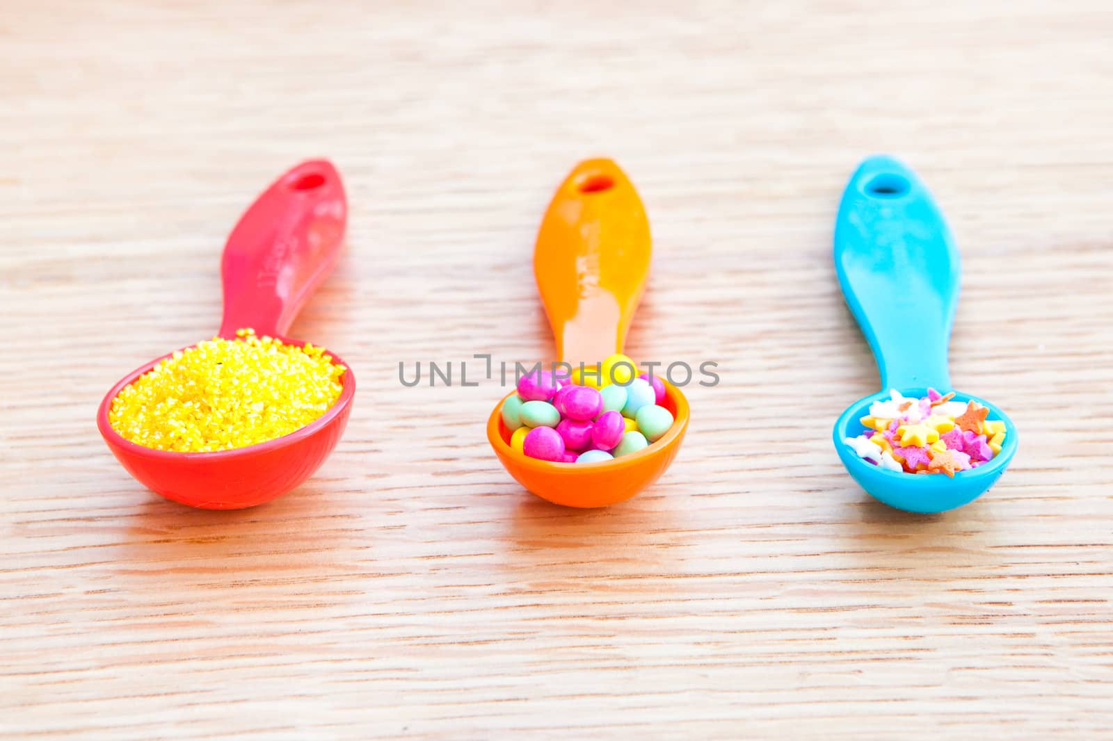 Three colorful plastic measuring spoons with cake decorations