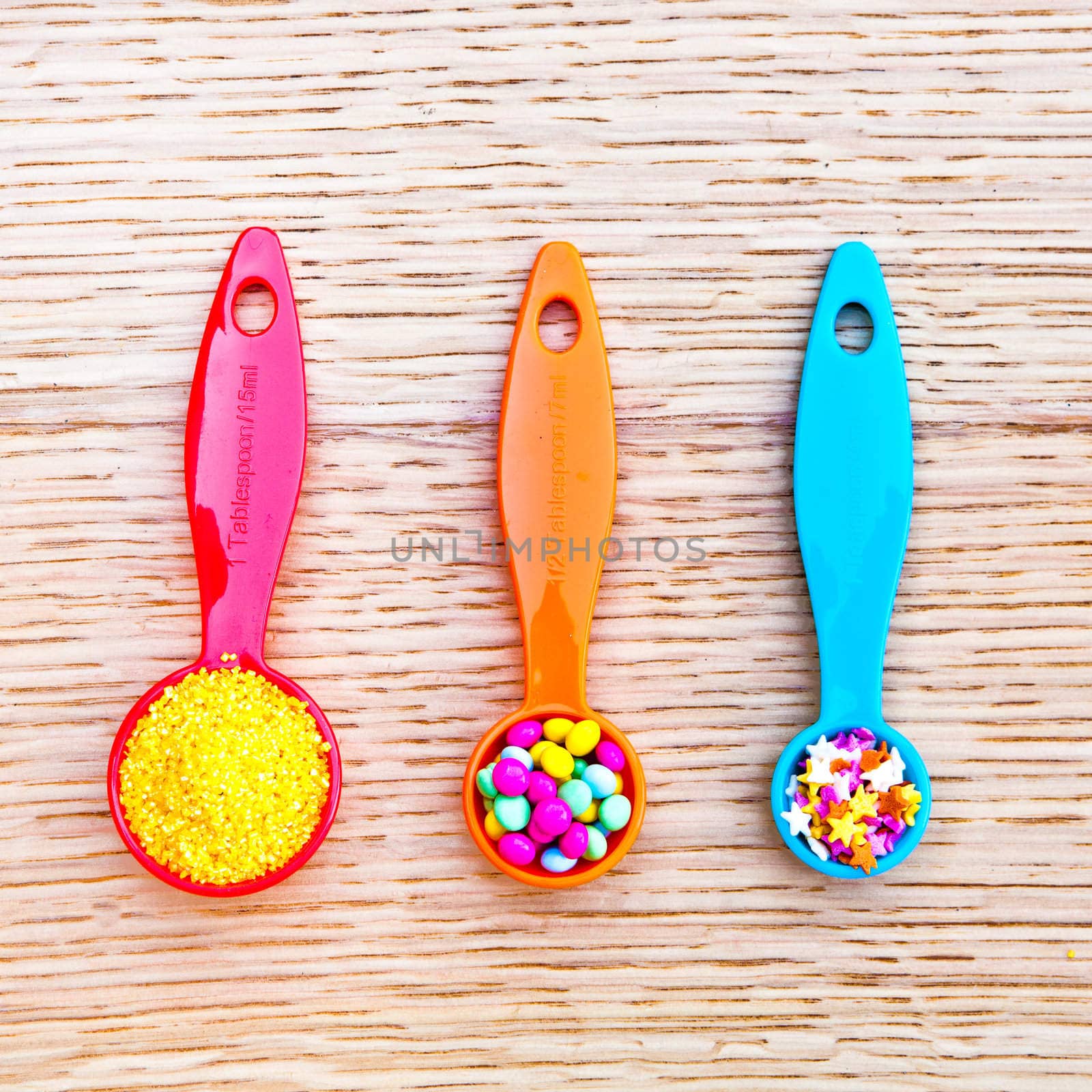 Three colorful plastic measuring spoons with cake decorations