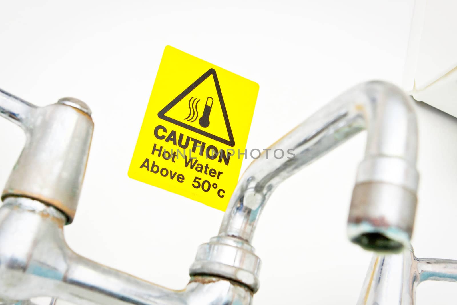 A bright yellow hot water warning notice behind a chrome tap