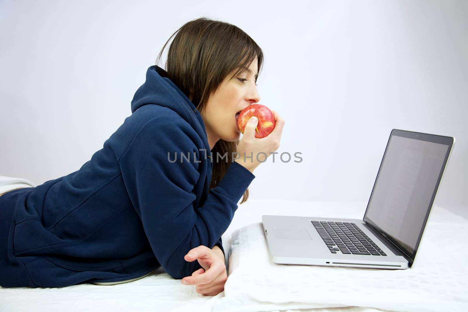 Woman eating happy an apple in front of computer laying in bed