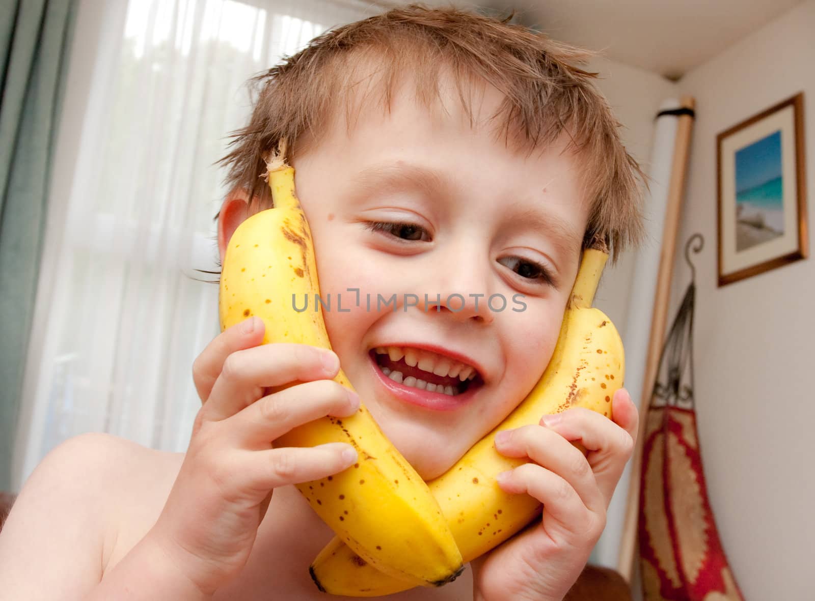 Cute little boy pretending to talk on the telephone using bananas