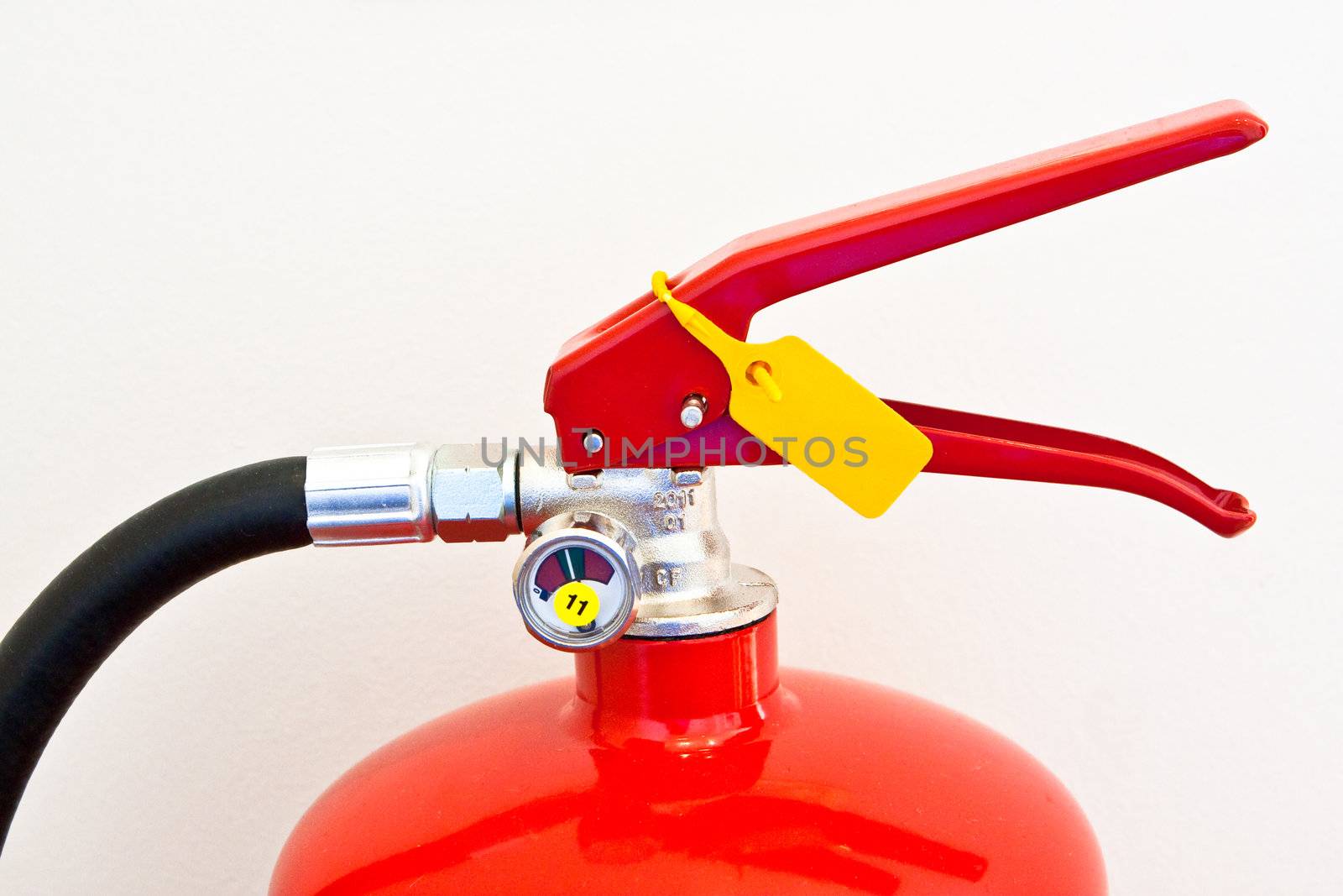 The top of a red fire extinguisher against a cream colored wall