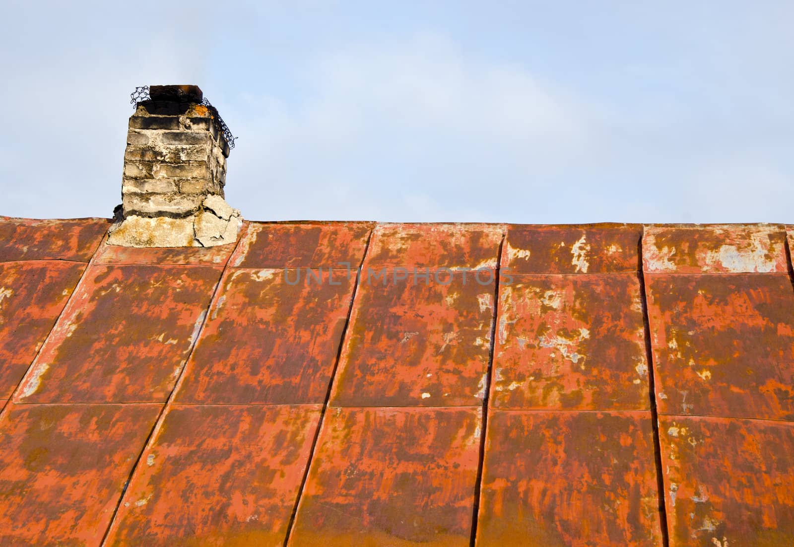 Roof made of rusty tin and ramshackle brick chimney of an old abandoned country house.