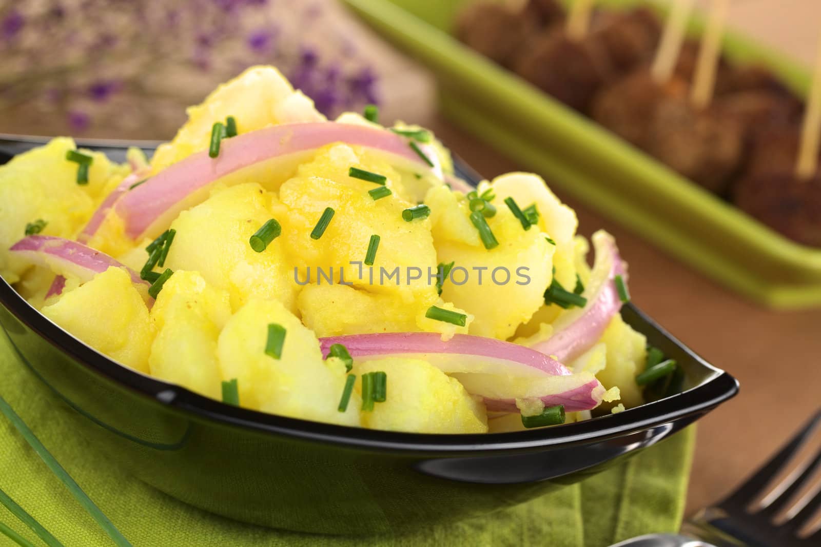 Potato salad with onions prepared in Swabian-Style (Southern Germany) garnished with chives, meatballs in the back (Selective Focus, Focus one third into the bowl)