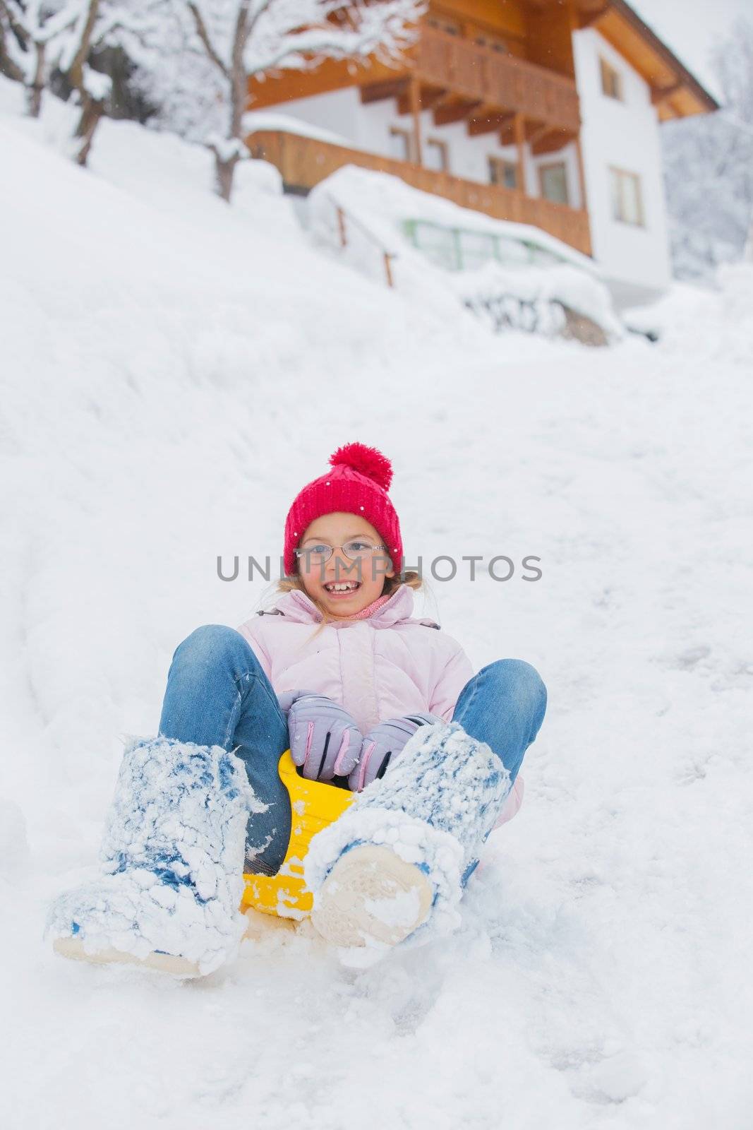 Cute pretty girl in red hat riding on a sled near the Austrian cottage