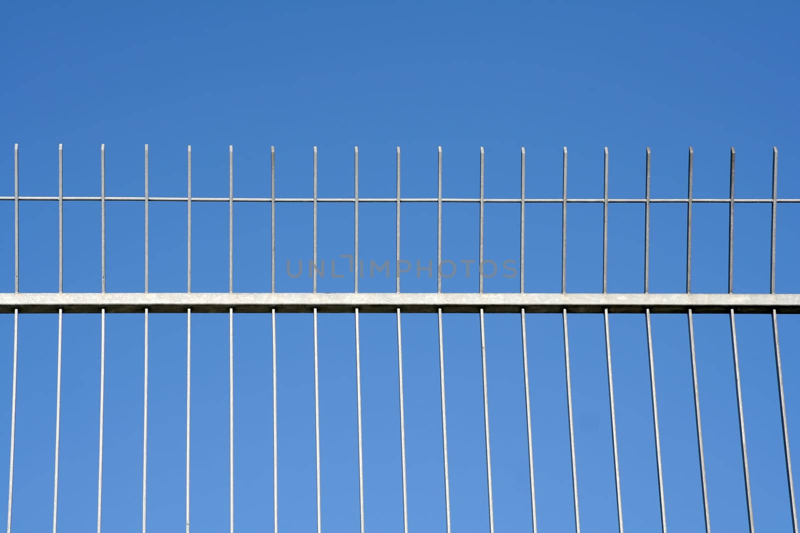 Metal fence against clear blue sky. No trespassing.
