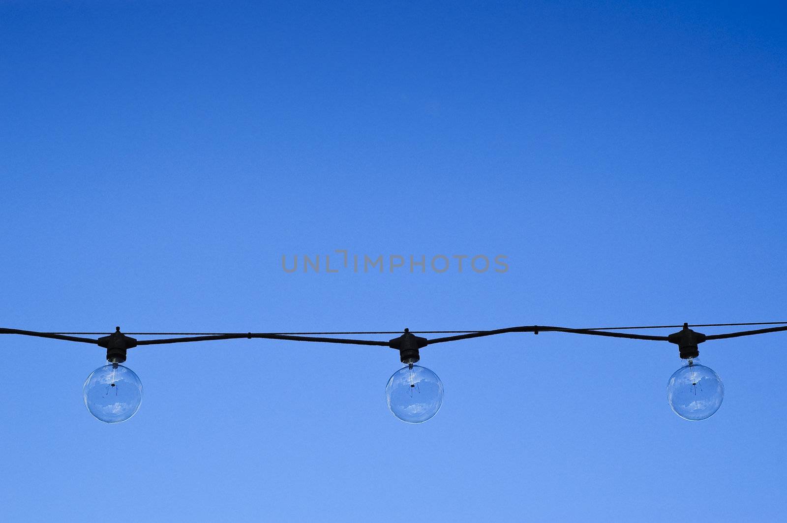 Three clear round light bulbs hanging against a blue summer sky