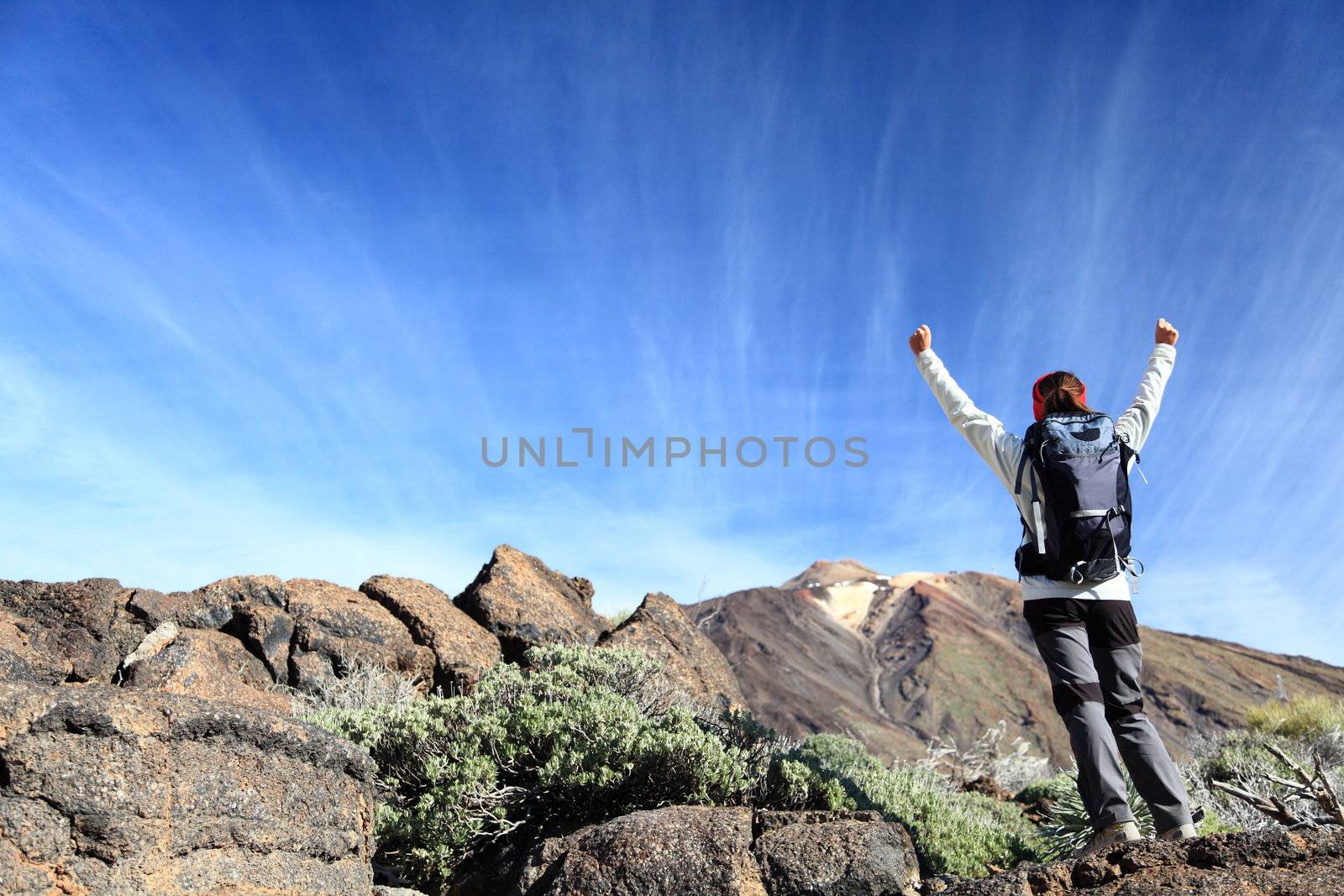 Hiker cheering. Happy hiking woman with arms raised overcoming challenges. From hike on volcano Teide, Tenerife, Canary Islands, Spain.