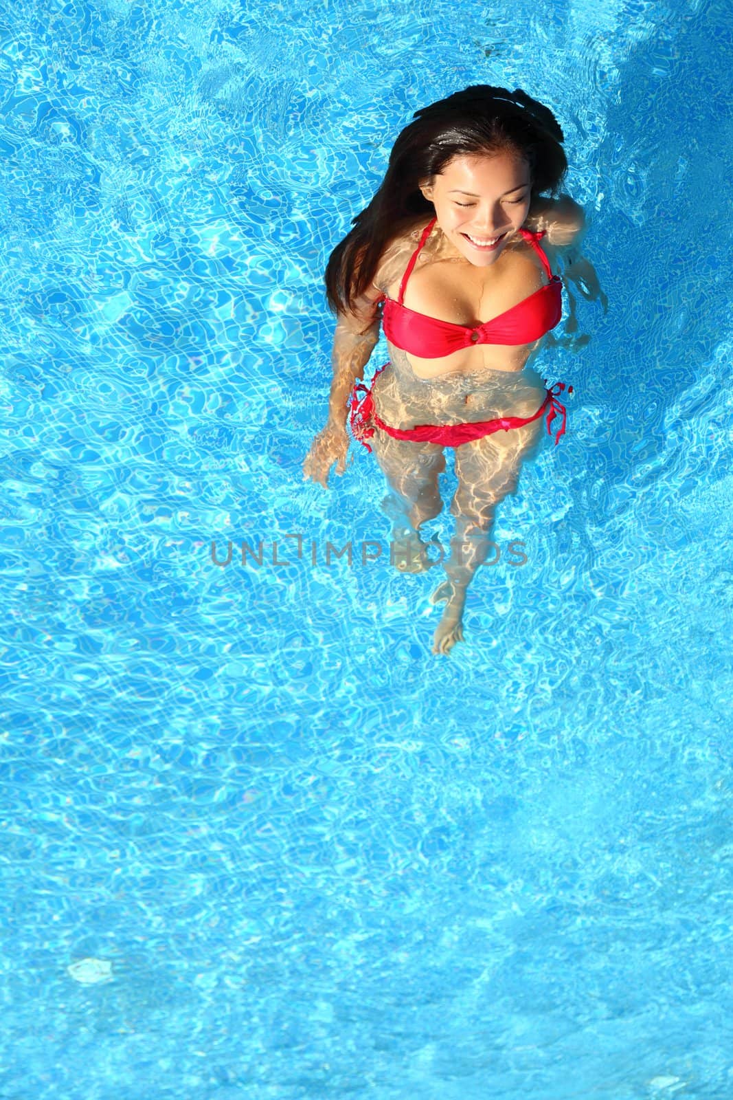 Woman relaxing in swimming pool. Beautiful gorgeous young bikini model bathing in blue swimming pool on resort during holiday. Pretty multiracial Asian / Caucasian woman in red bikini.