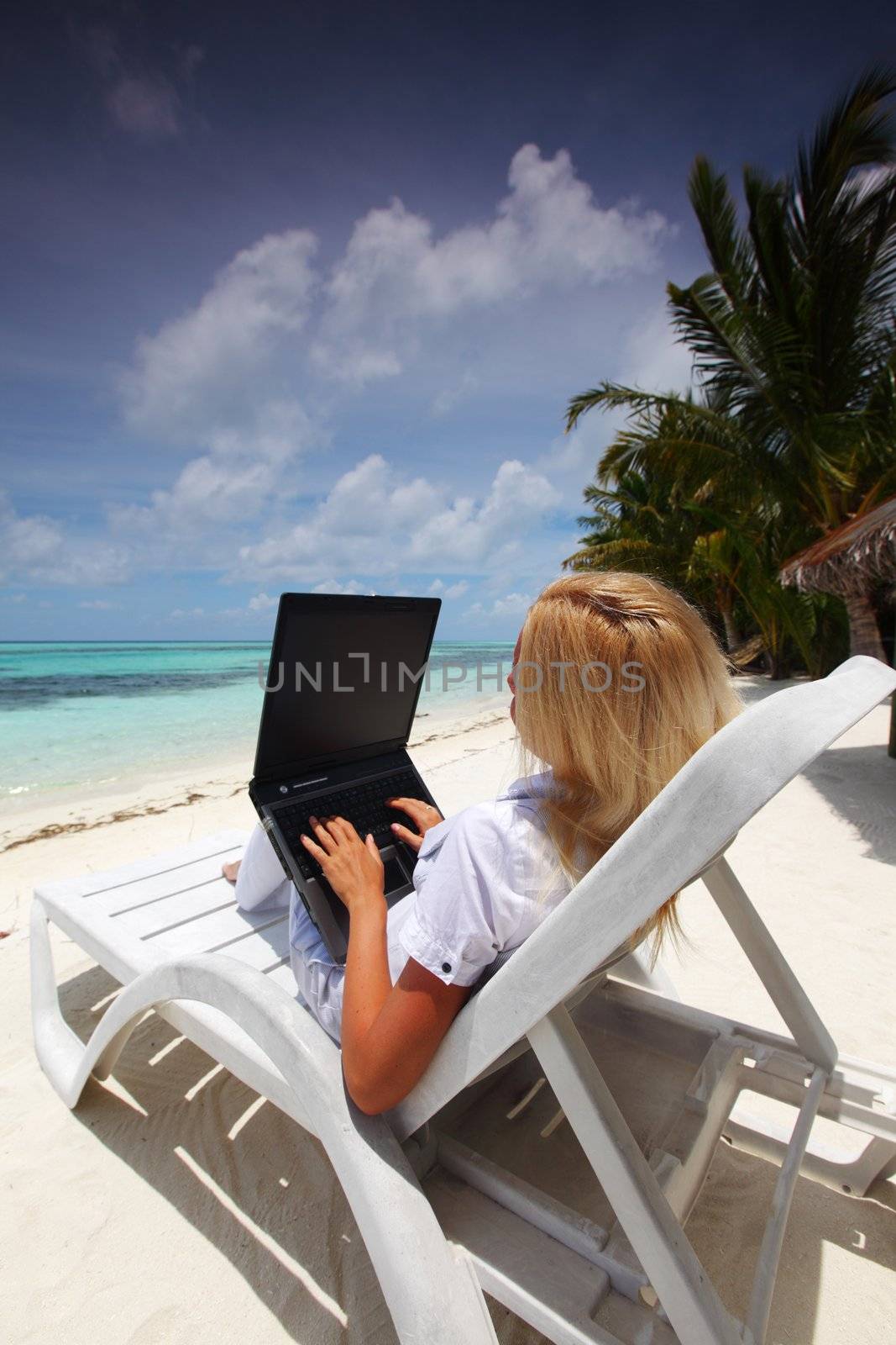 business woman with laptop lying on a chaise lounge in the tropical ocean coast