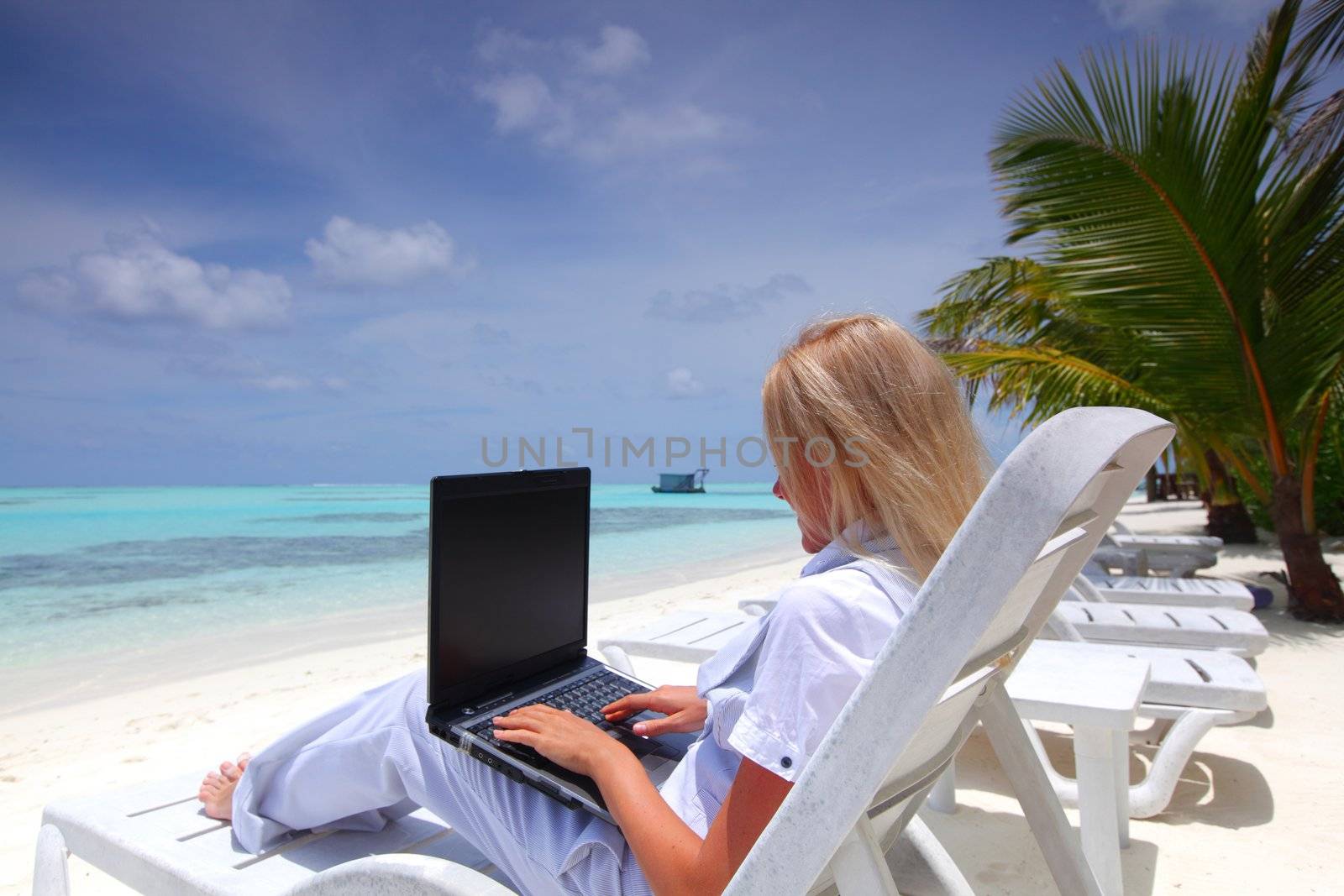 business woman with laptop lying on a chaise lounge in the tropical ocean coast