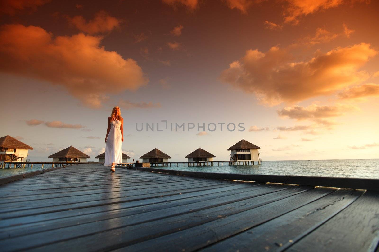 woman in a dress on a bridge home sea and the maldivian sunset on the background