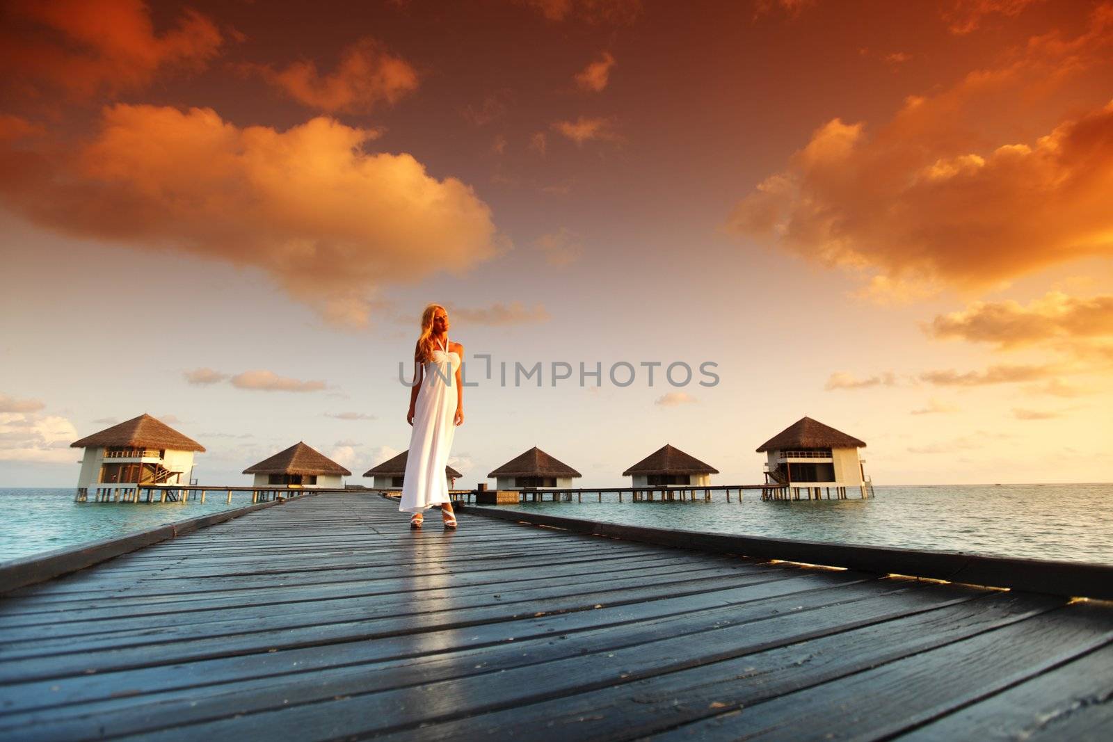 woman in a dress on a bridge home sea and the maldivian sunset on the background