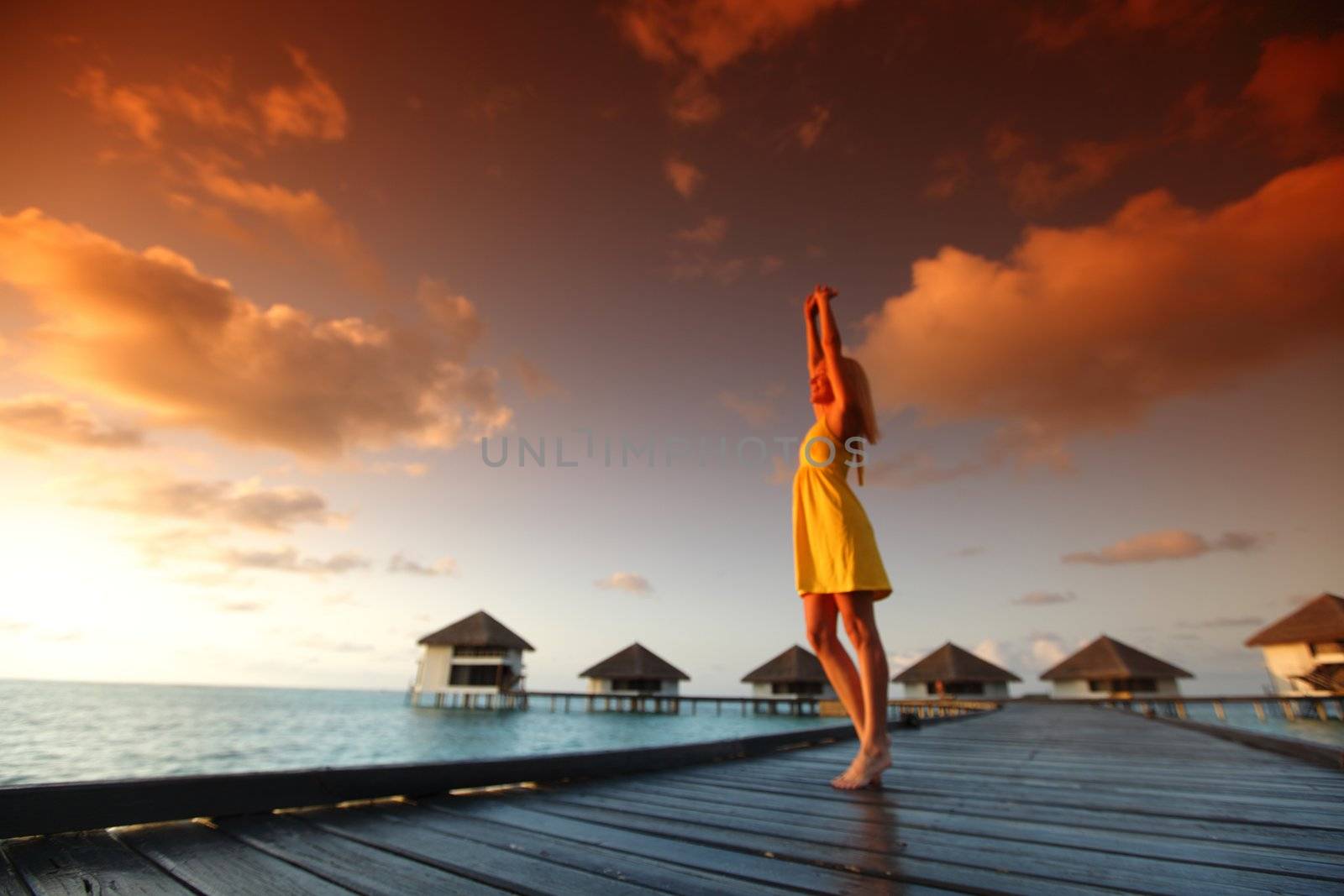 woman in a dress on a bridge home sea and the maldivian sunset on the background