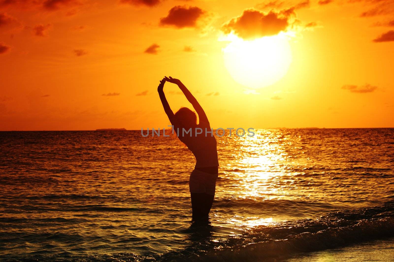 happy woman standing on a sunset in ocean waves