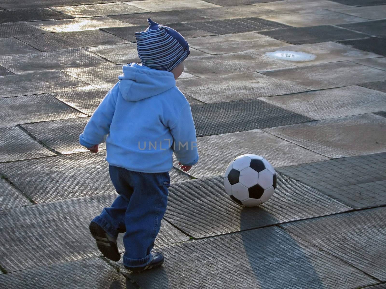 Little child playing soccer ball outdoors