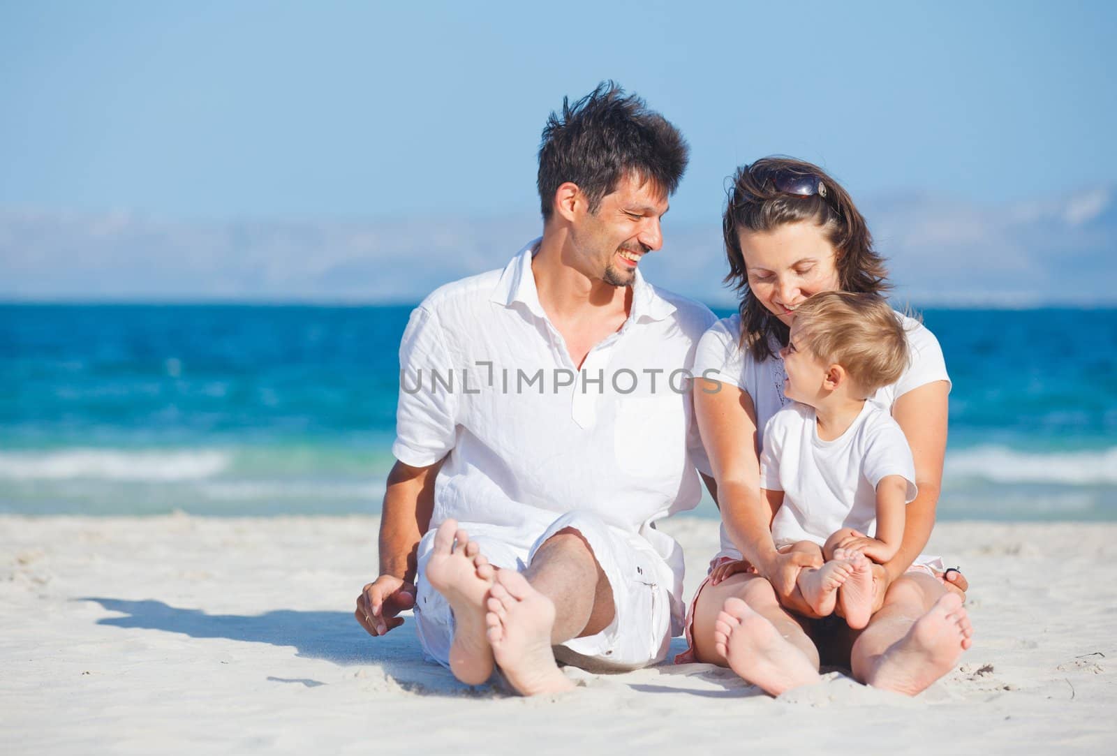 Happy family of three sitting and having fun on tropical beach
