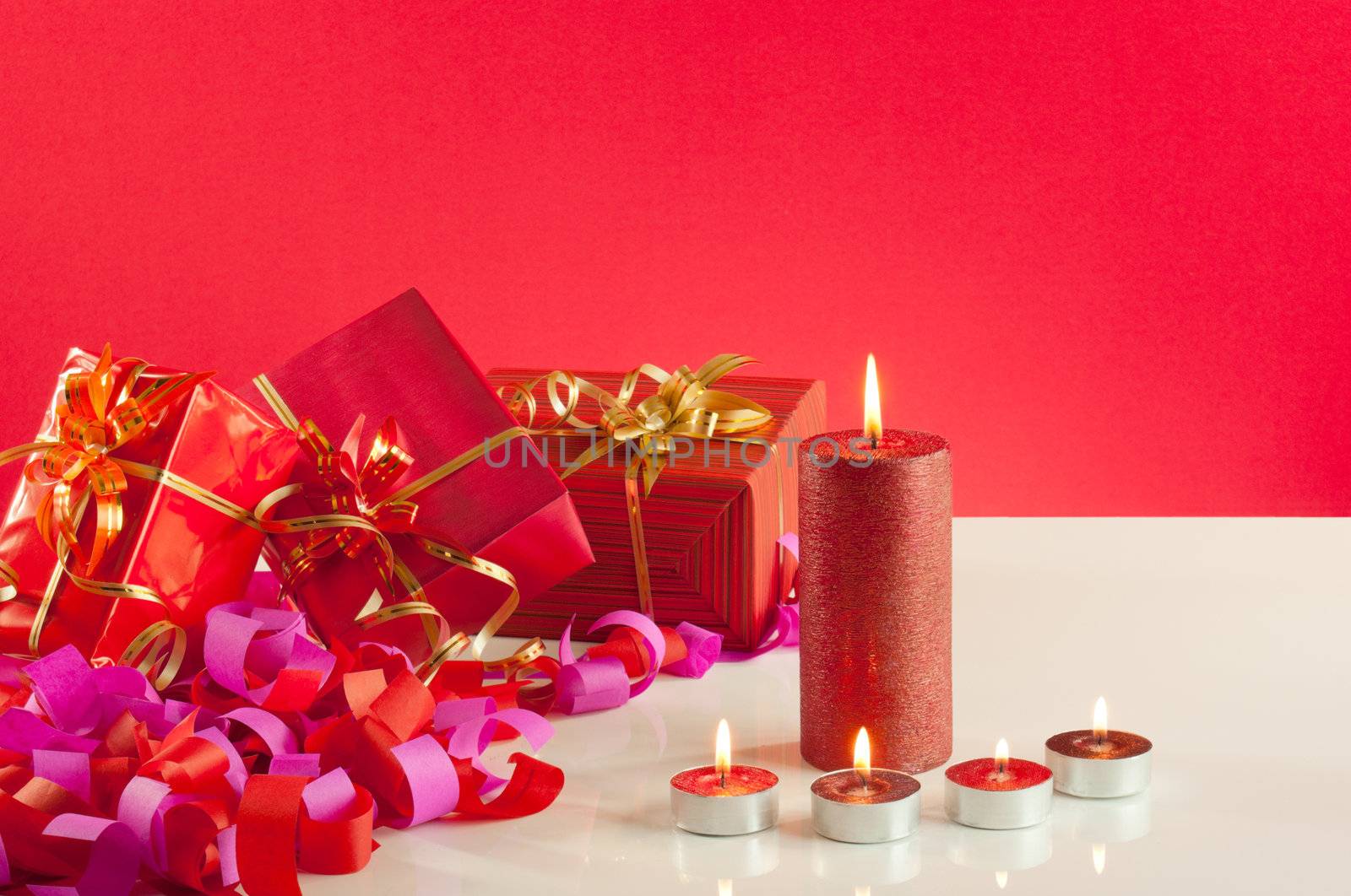 Christmas gifts and candles over red background