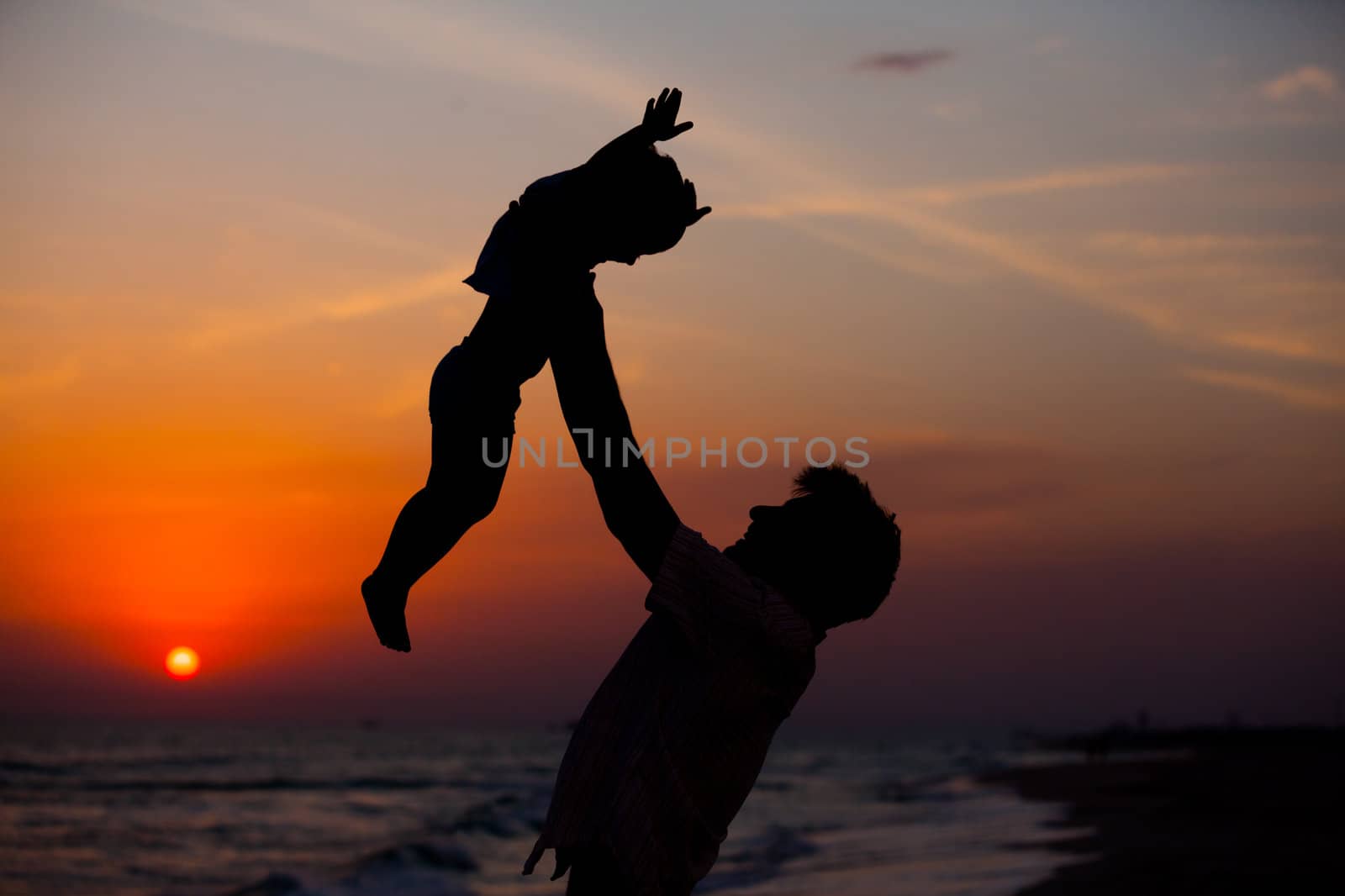 Father and little son silhouettes on beach at sunset