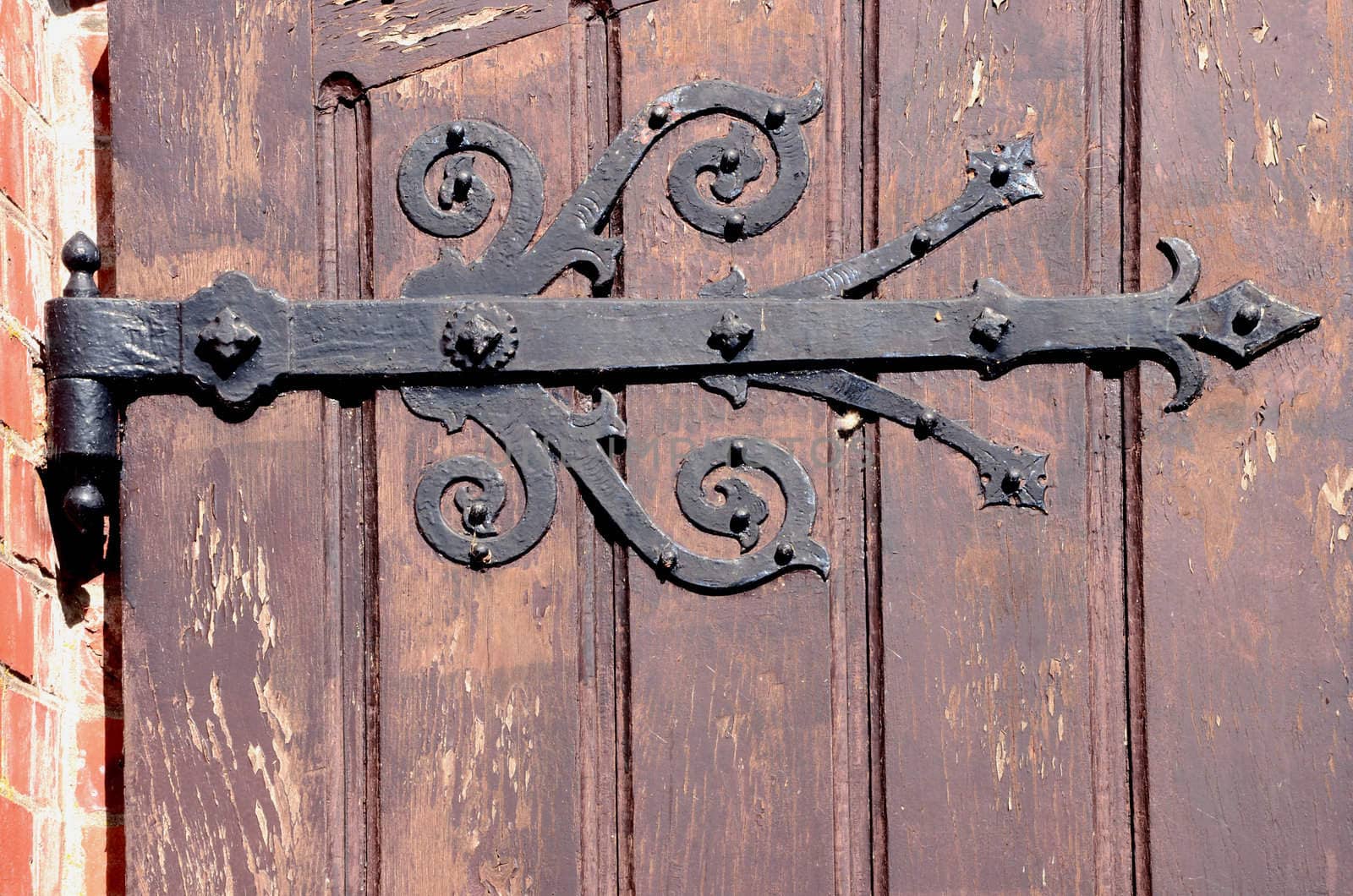 Detail of old decorative hinges holding wooden door. Architectural backdrop fragment.