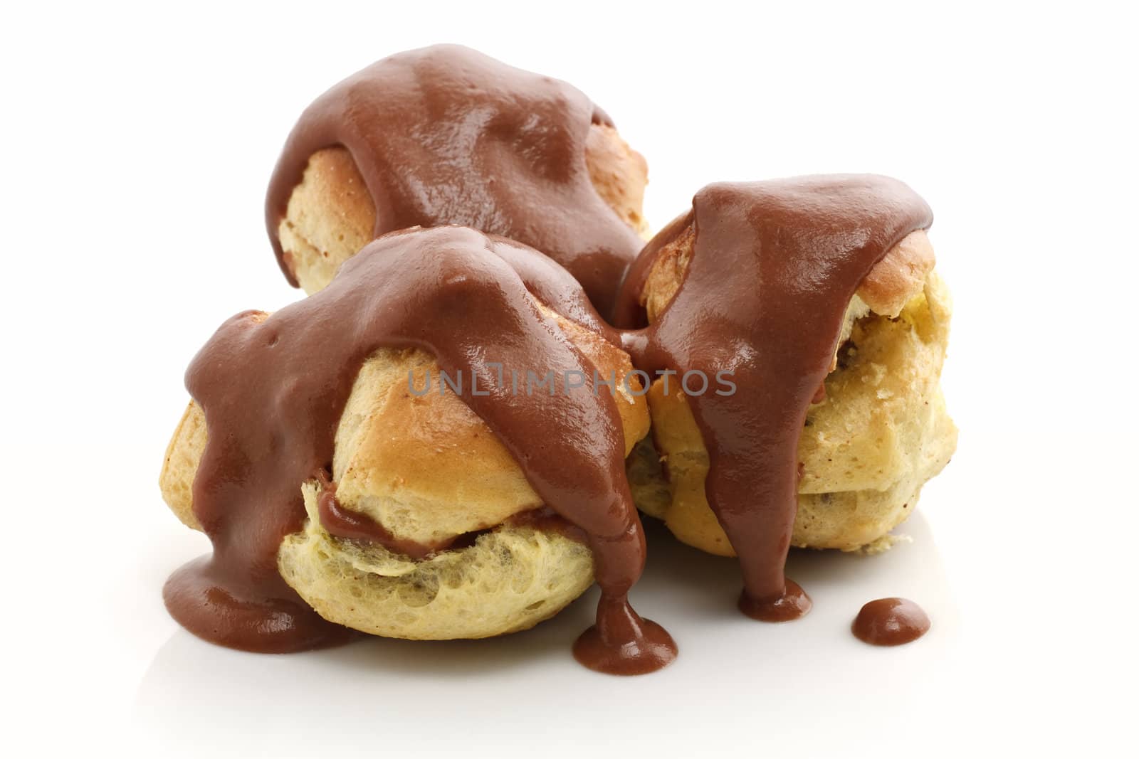 three profiteroles with chocolate sauce over white background