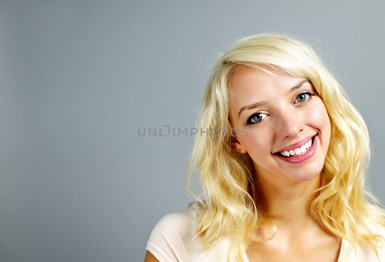 Portrait of smiling young blonde caucasian woman on grey background