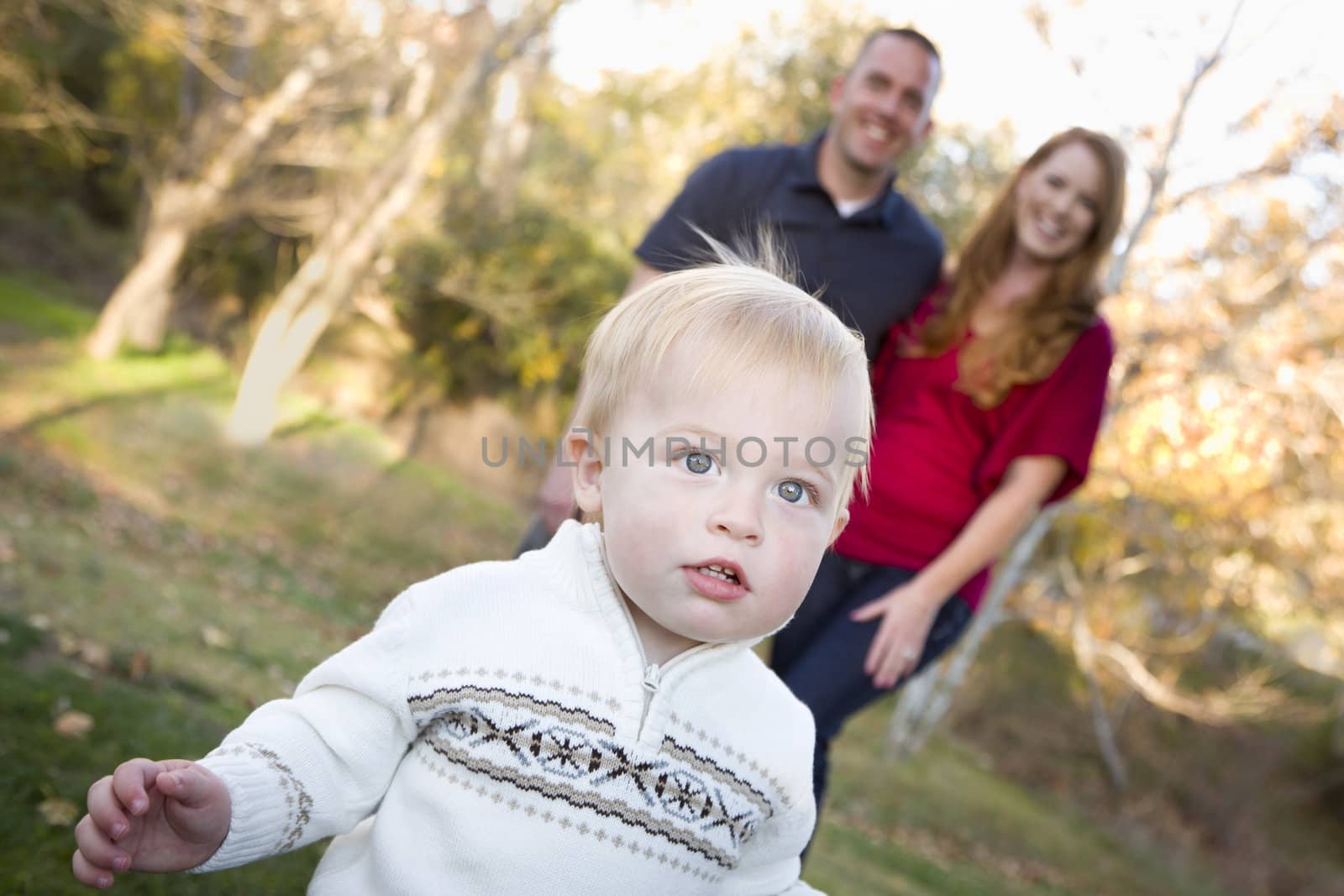 Cute Young Boy Walking in the park as Adoring Parents Look On From Behind.