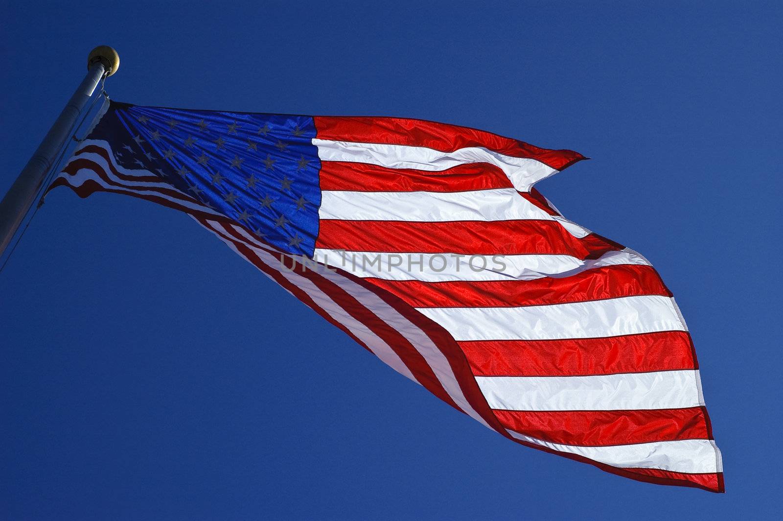 Backlit american flag blowing in the wind against blue skies