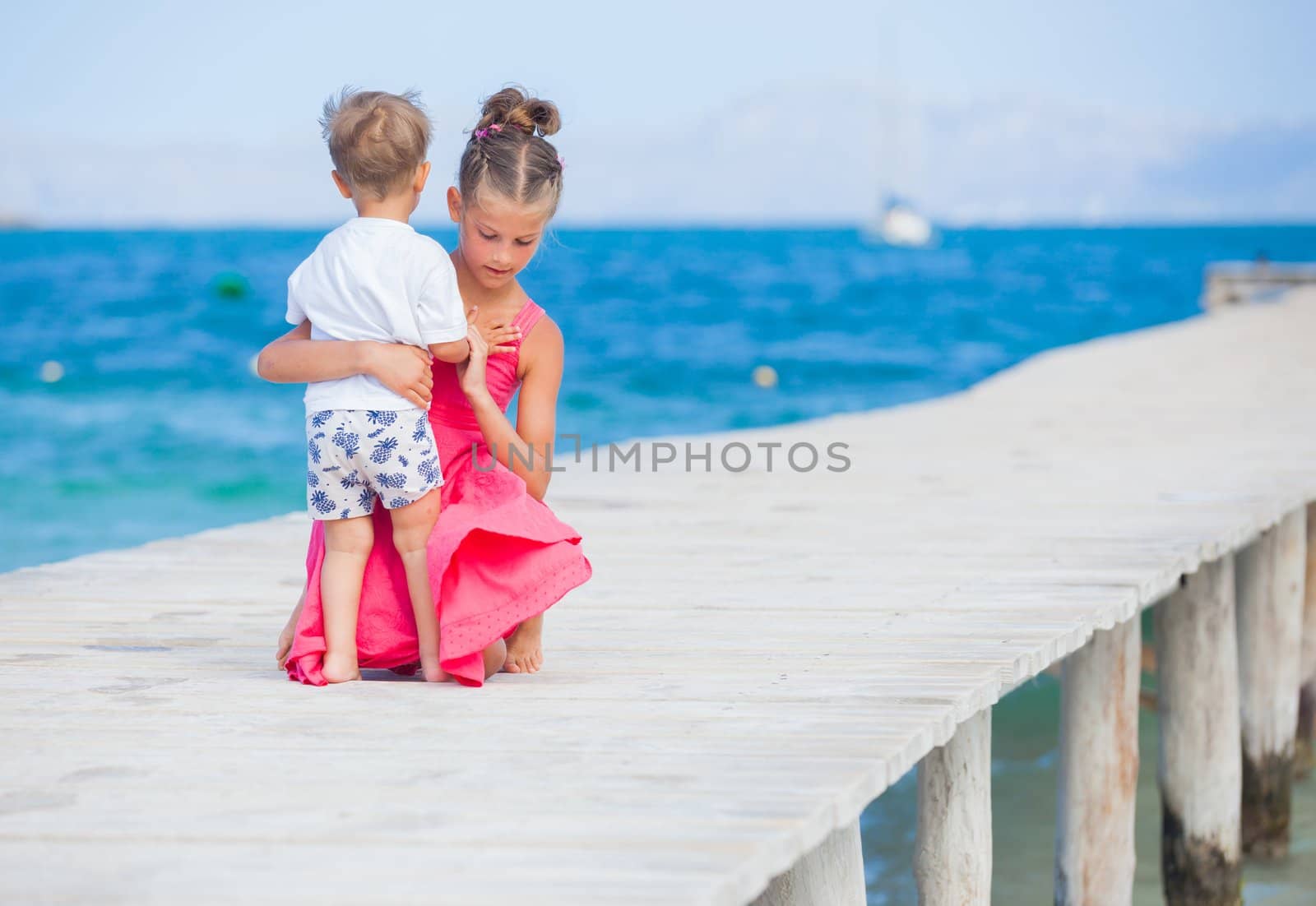 Back view of cute girl with her brother walking on jetty with turquoise sea