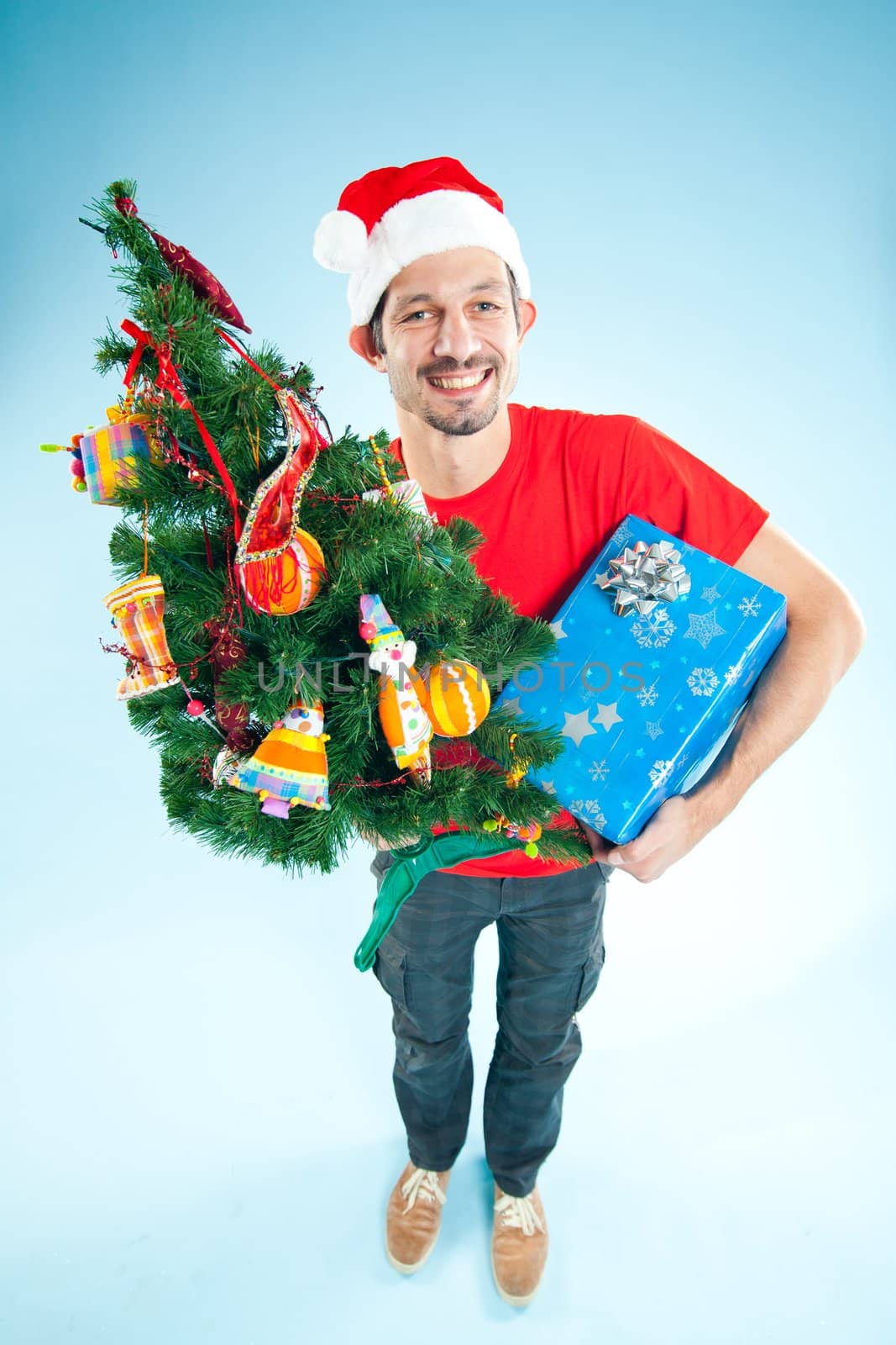 Happy smile young man in Santa hat with gifts and a Christmas tree