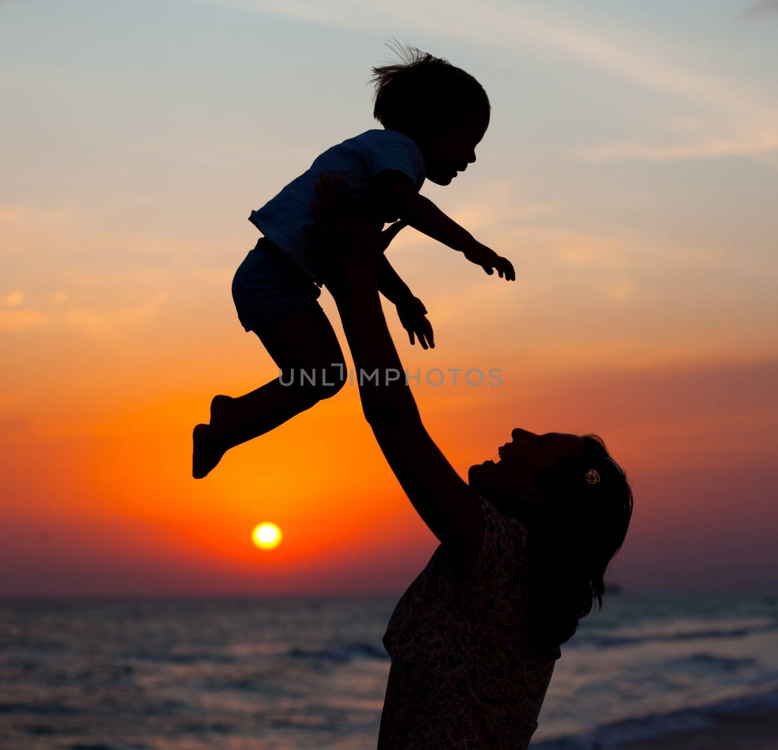 Mother and little son silhouettes on beach at sunset