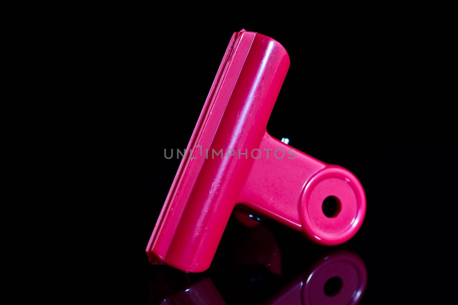 close up view of a  pink clamp on a mirror with dark background and mirror image
