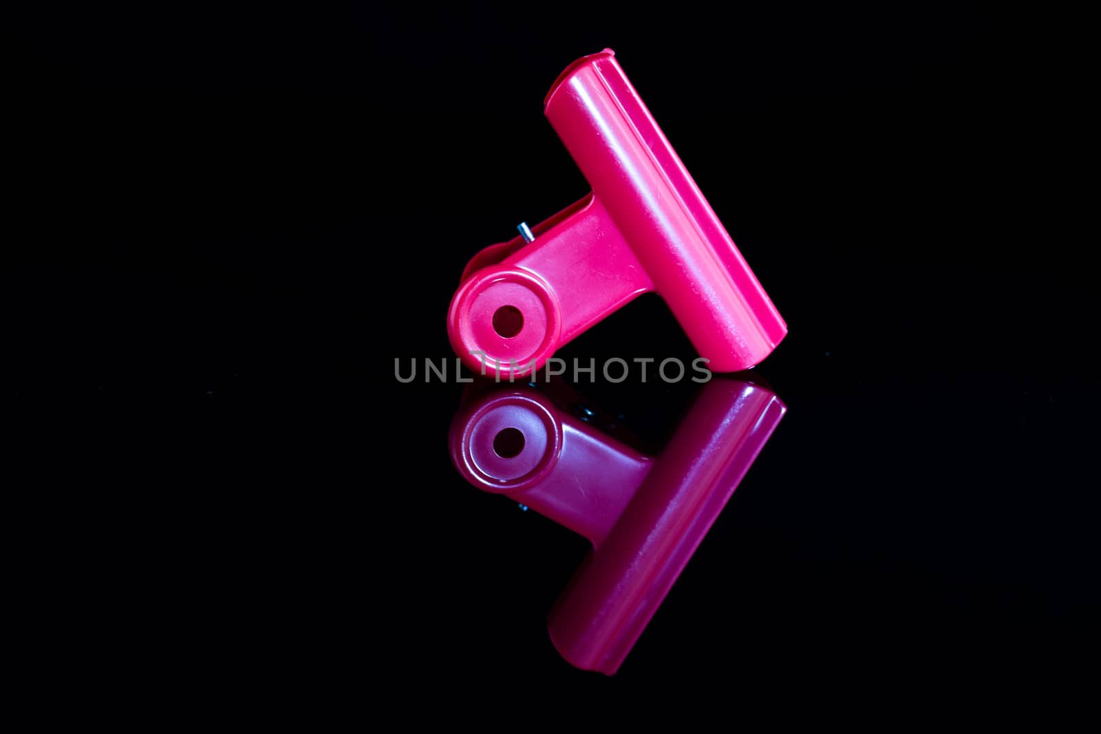 One pink clamp on a mirror with dark background ind mirror image