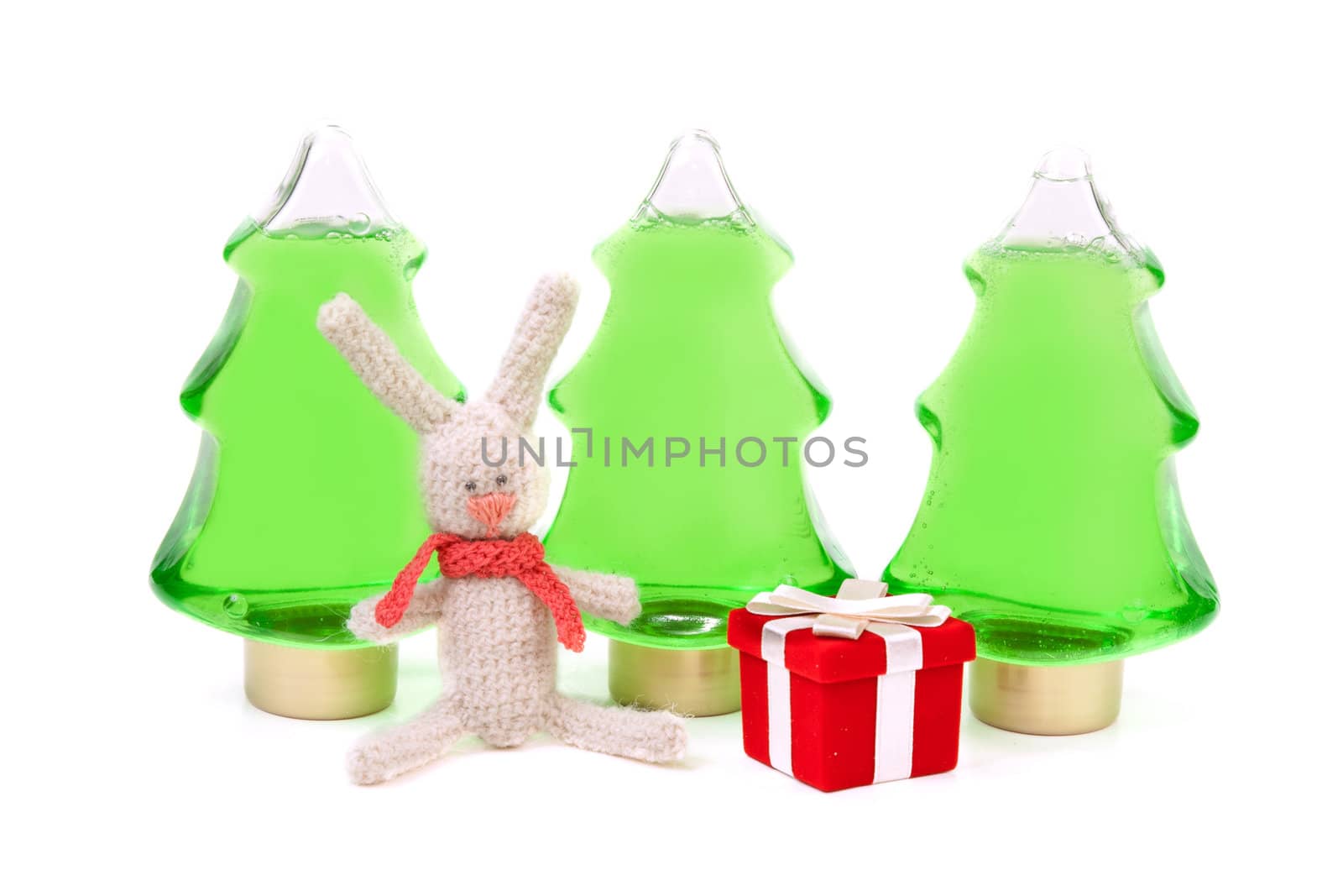 Knitted rabbit and a red box gifts to the background of three green bottles in the shape of a Christmas tree