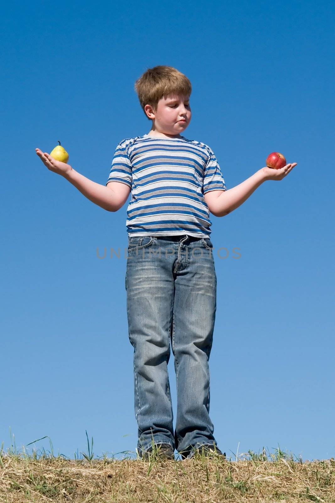 Difficult selection. Apple or pear? Boy with sky at background.
