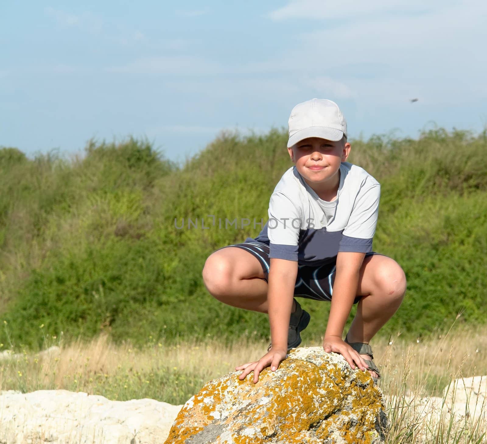 little boy sitting on a big rock