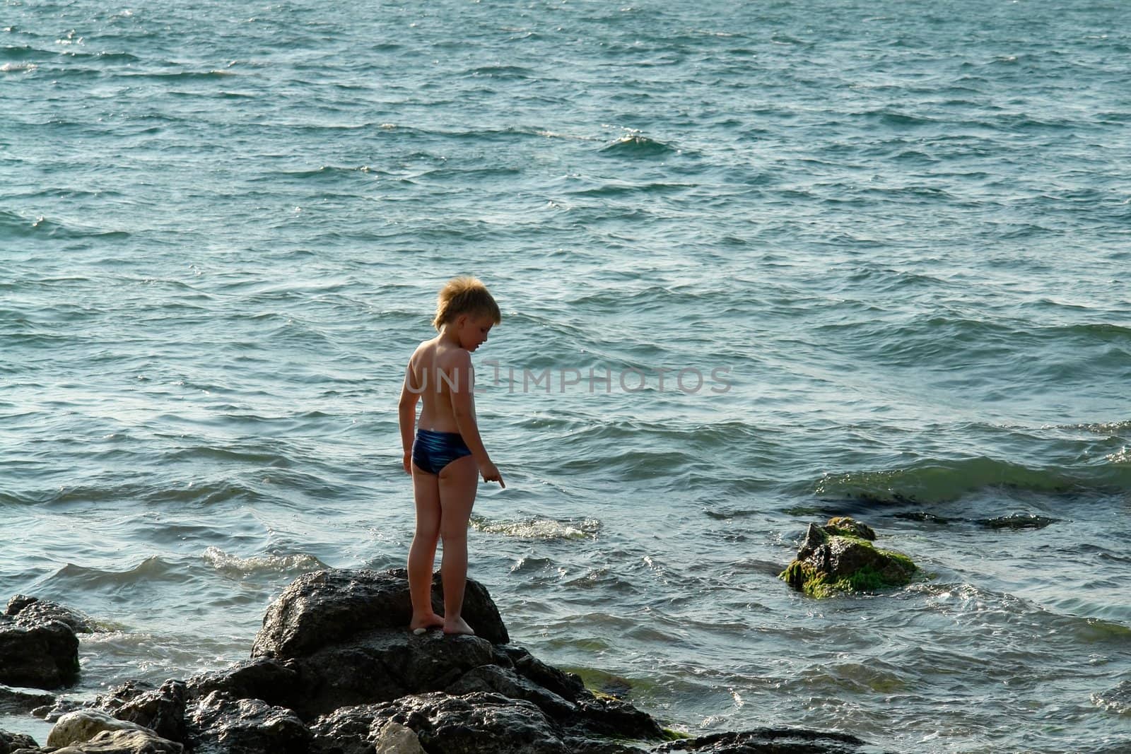 little boy on a rock in sea waves