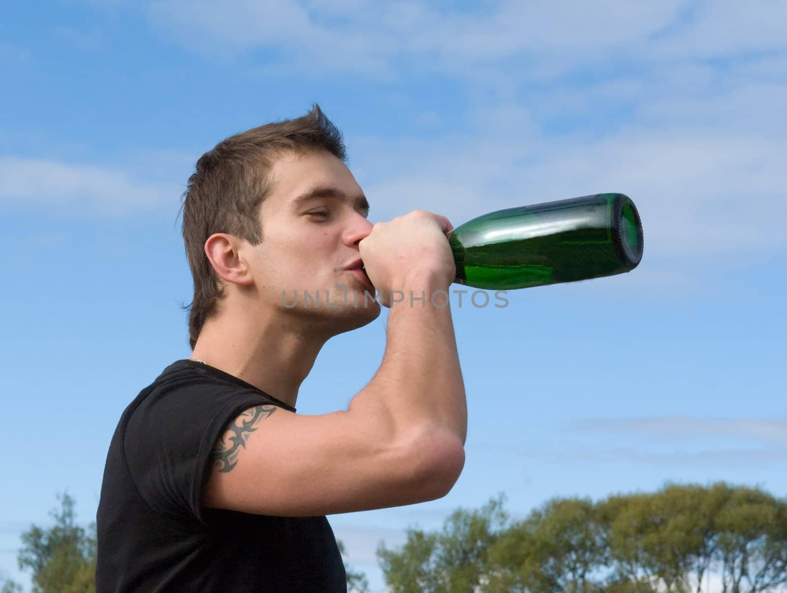 The young man drinks wine against the sky