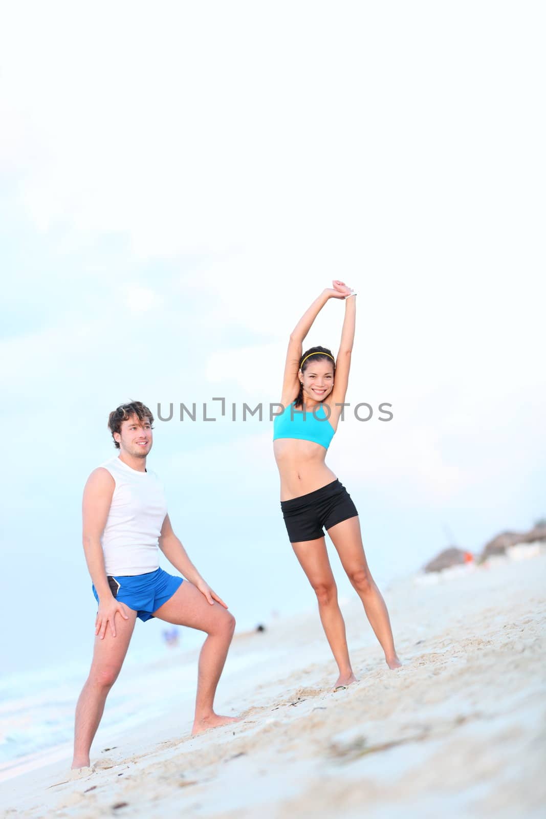 Workout couple exercising and stretching on beach. Young interracial couple, Asian woman, Caucasian man working out outdoor.